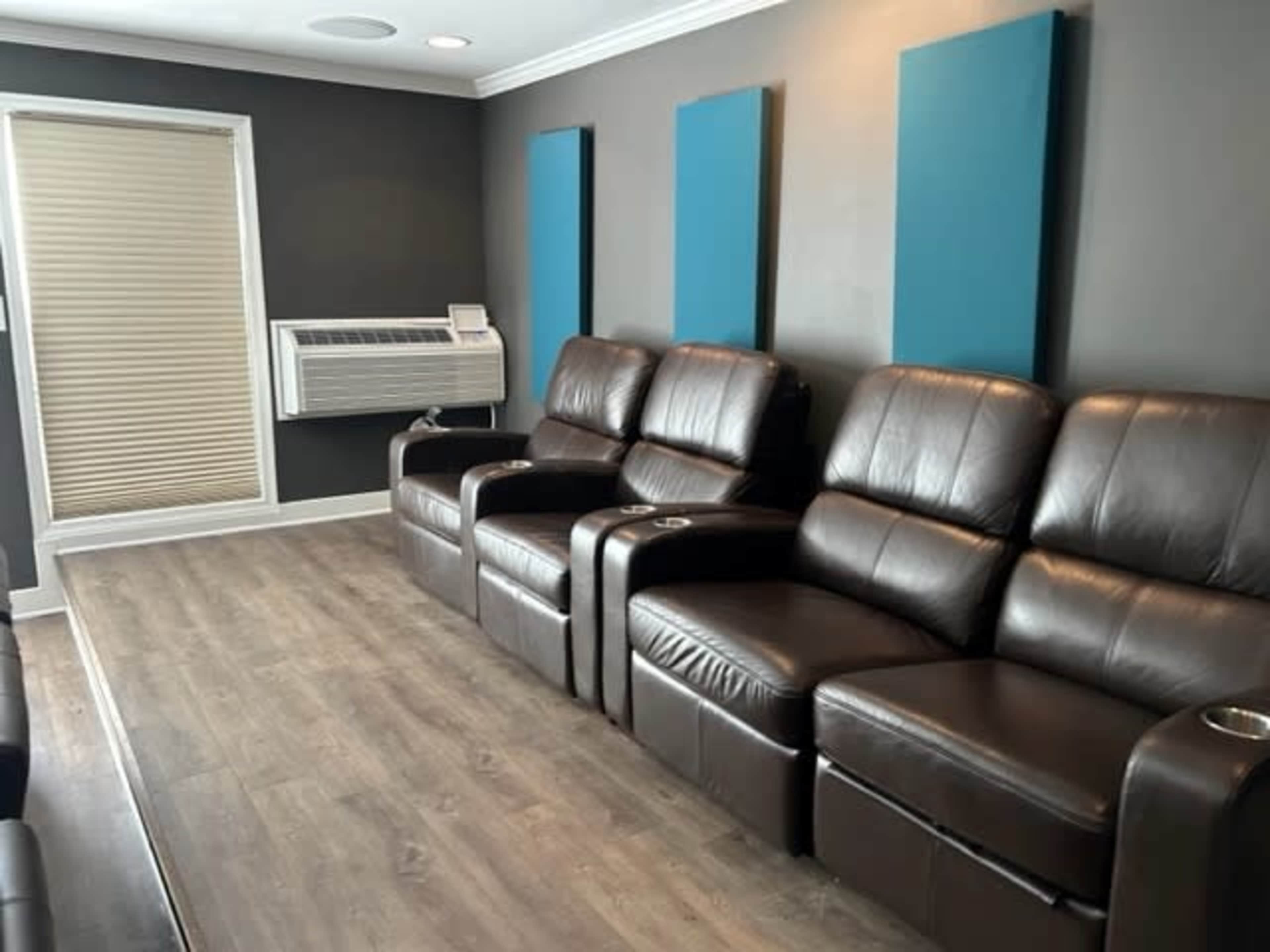 A row of dark leather reclining chairs in a room with gray walls and an air conditioning unit.