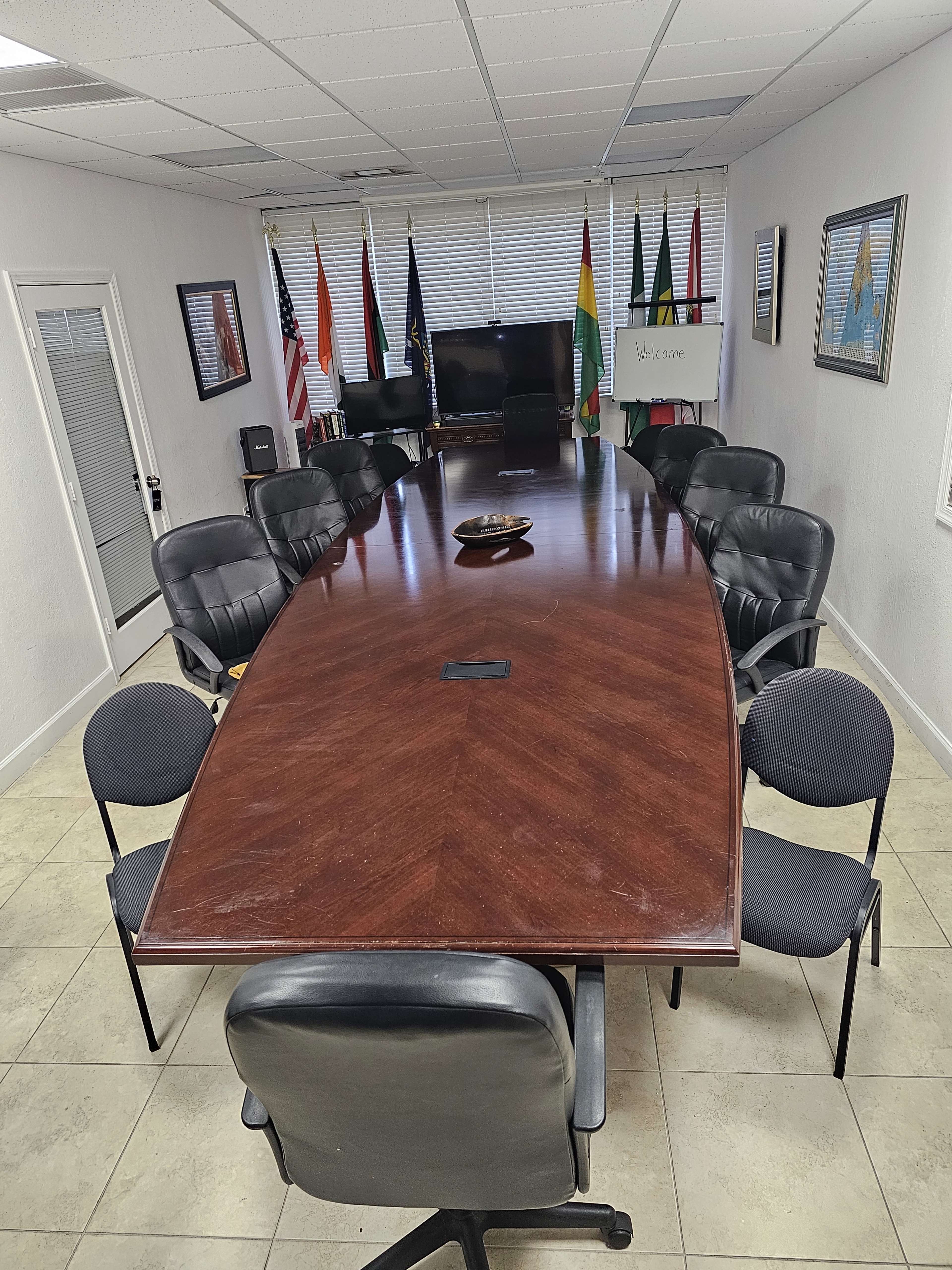 A large, elongated conference table surrounded by black chairs in a well-lit meeting room decorated with flags and framed artwork.
