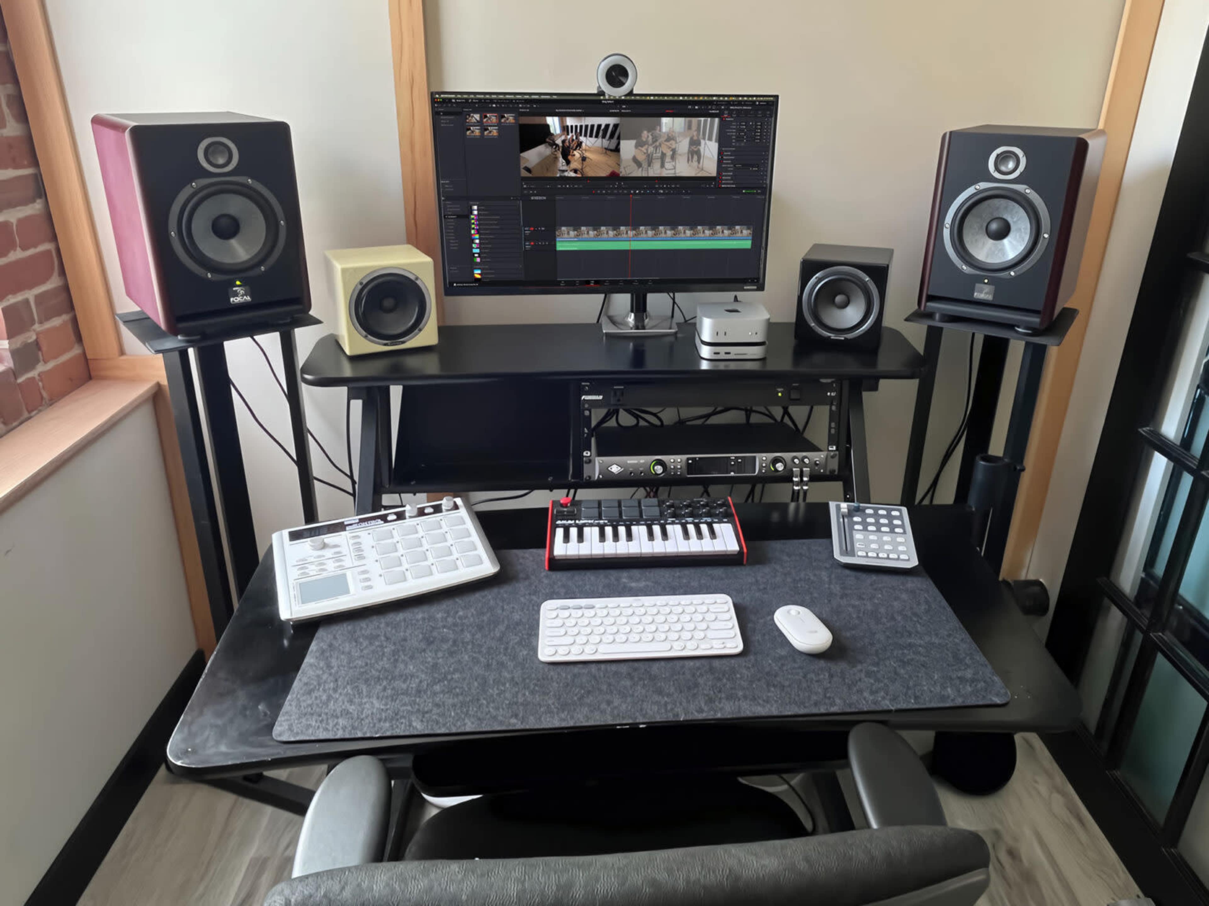 A well-organized music production workspace features a computer monitor displaying editing software, various audio speakers, and MIDI controllers on a sleek black desk.