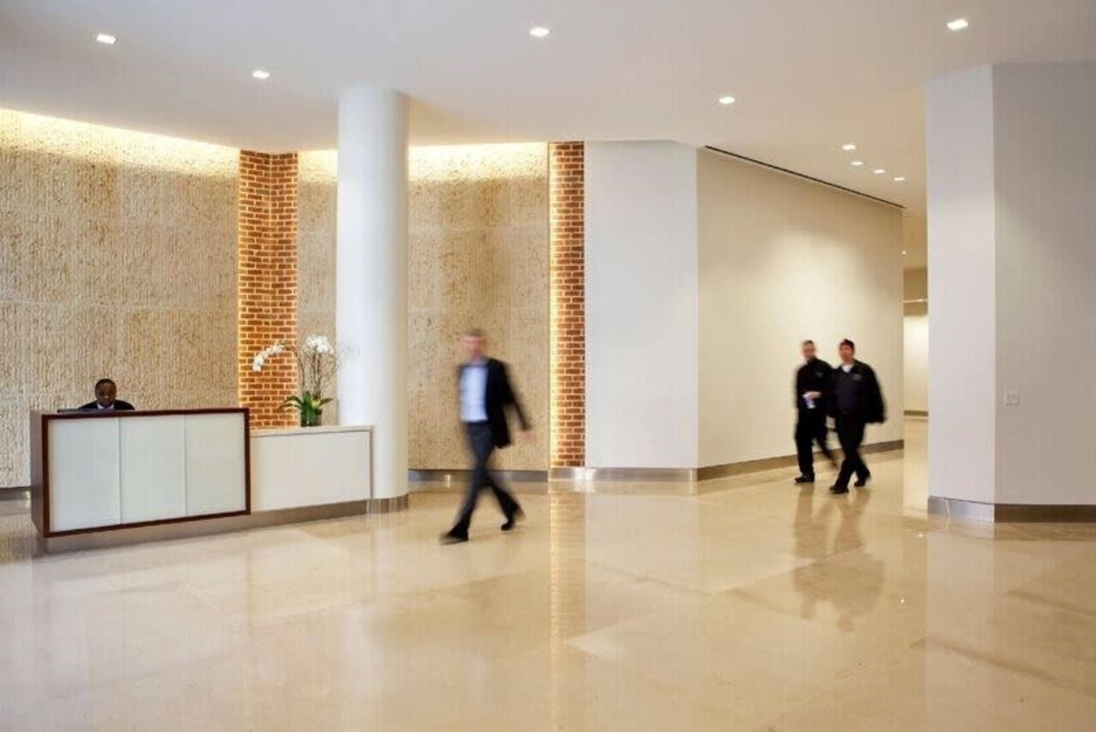 A modern reception area features a desk with a receptionist and three individuals walking through the space.