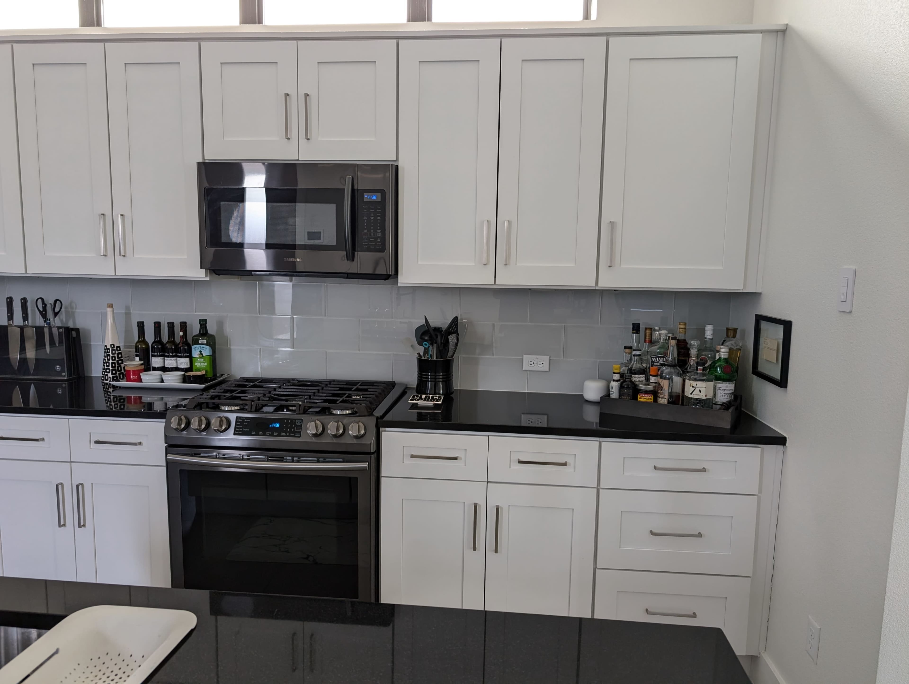 A modern kitchen features white cabinets, a stainless steel microwave, a gas stove, and a bar cart with various bottles of spirits.