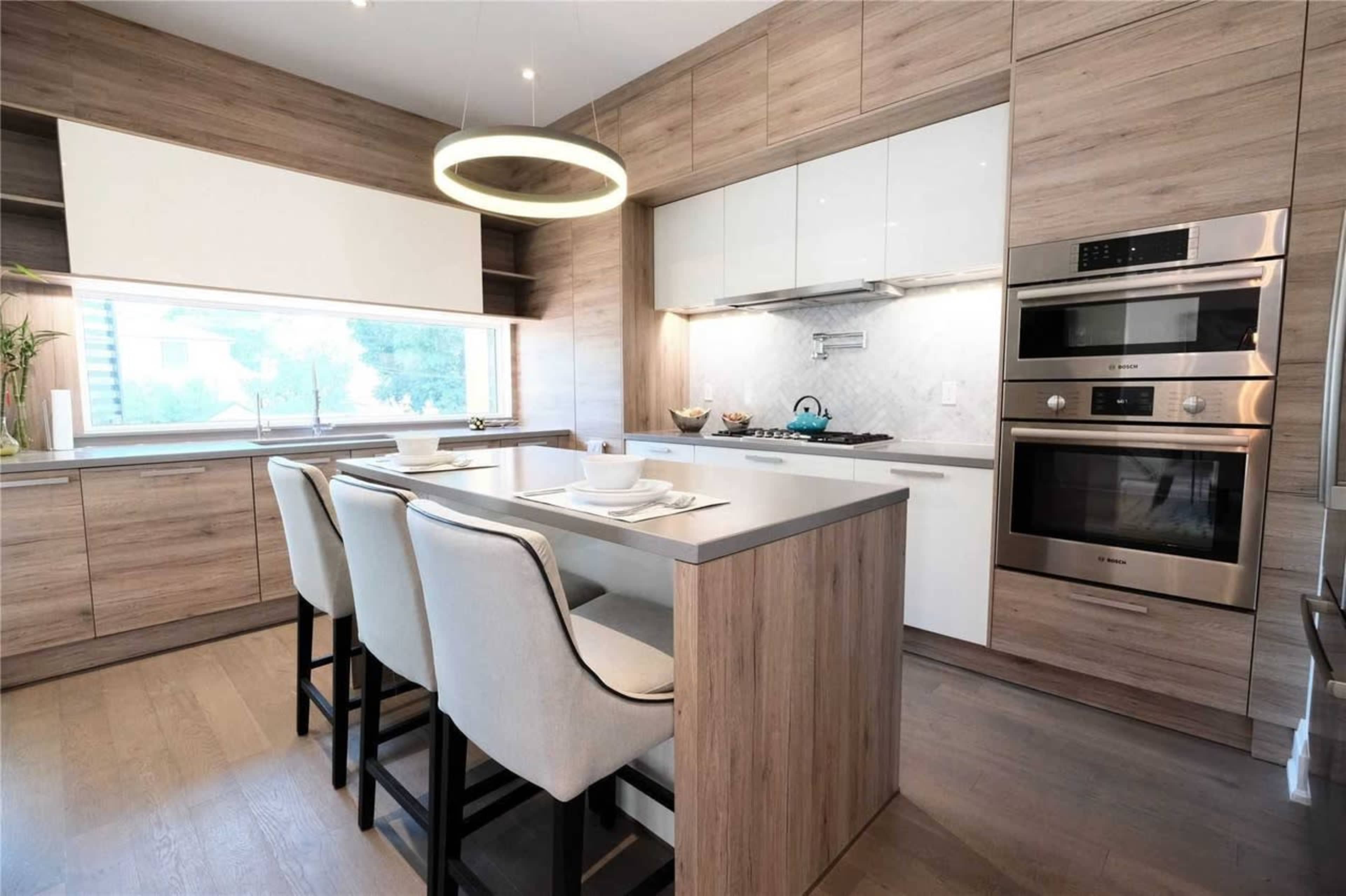 A modern kitchen features a central island with seating, sleek cabinetry, and built-in appliances against a backdrop of wood paneling.