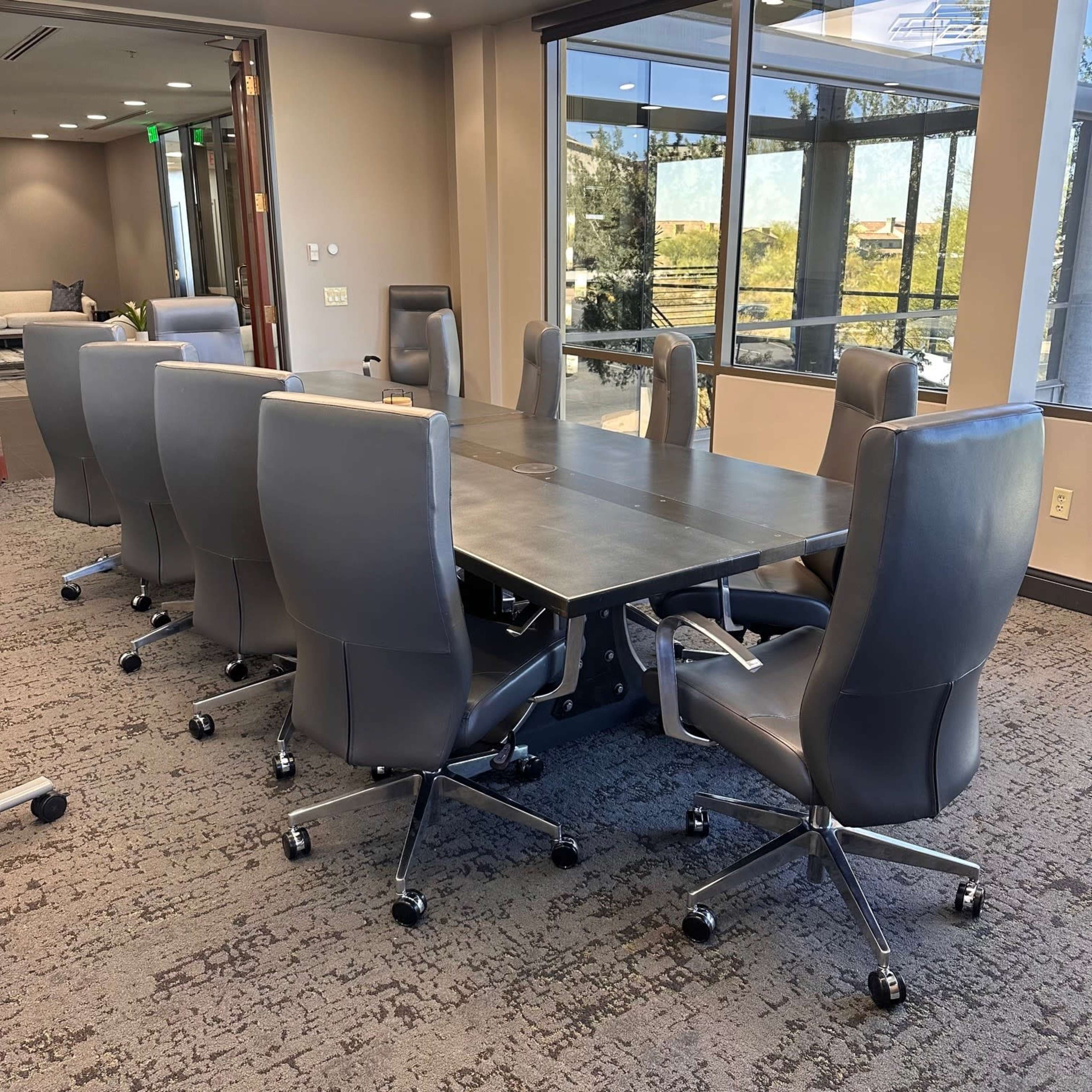 A modern conference room features a long table surrounded by eight gray office chairs.