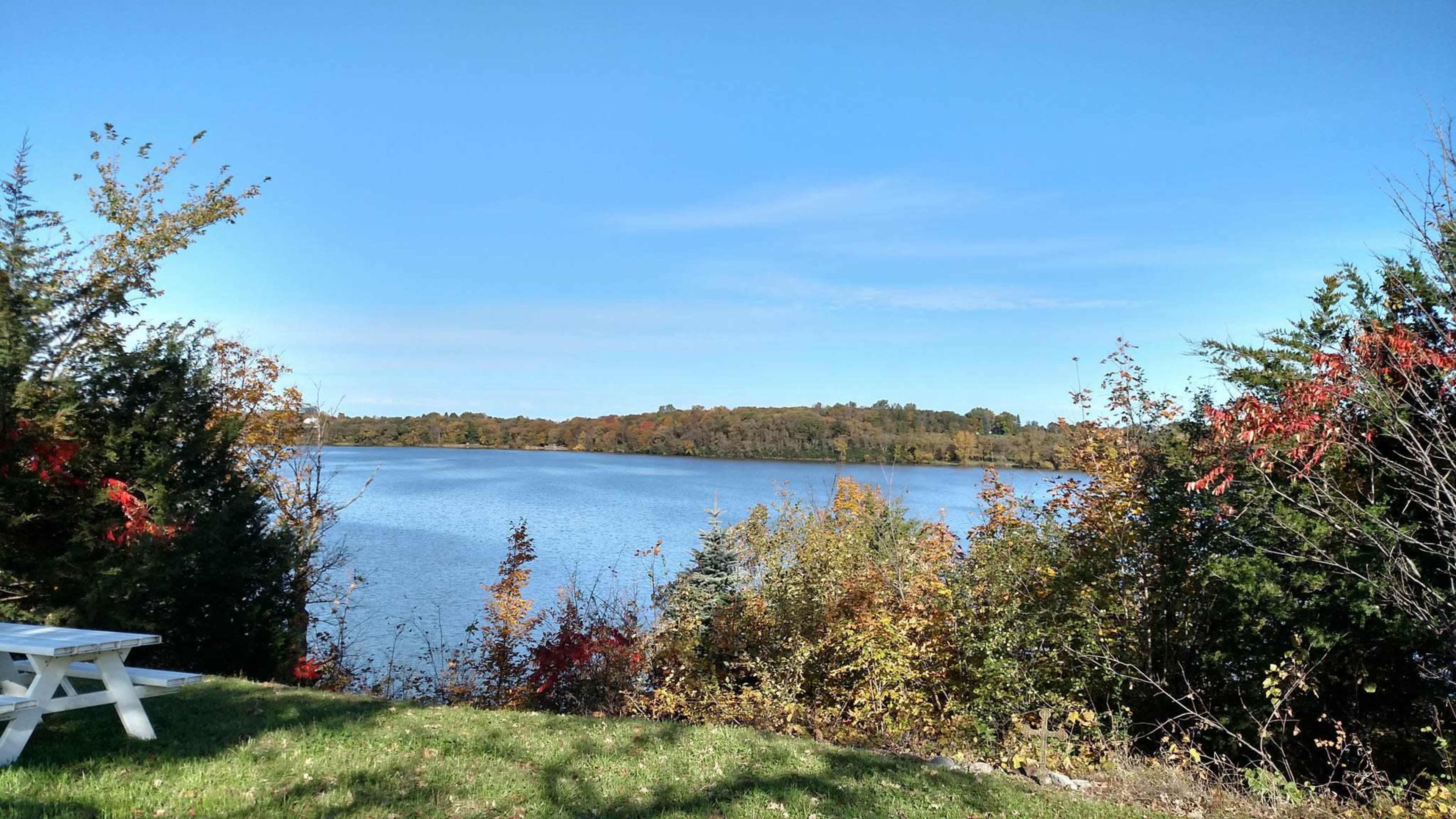 A tranquil lake is surrounded by colorful foliage under a clear blue sky.
