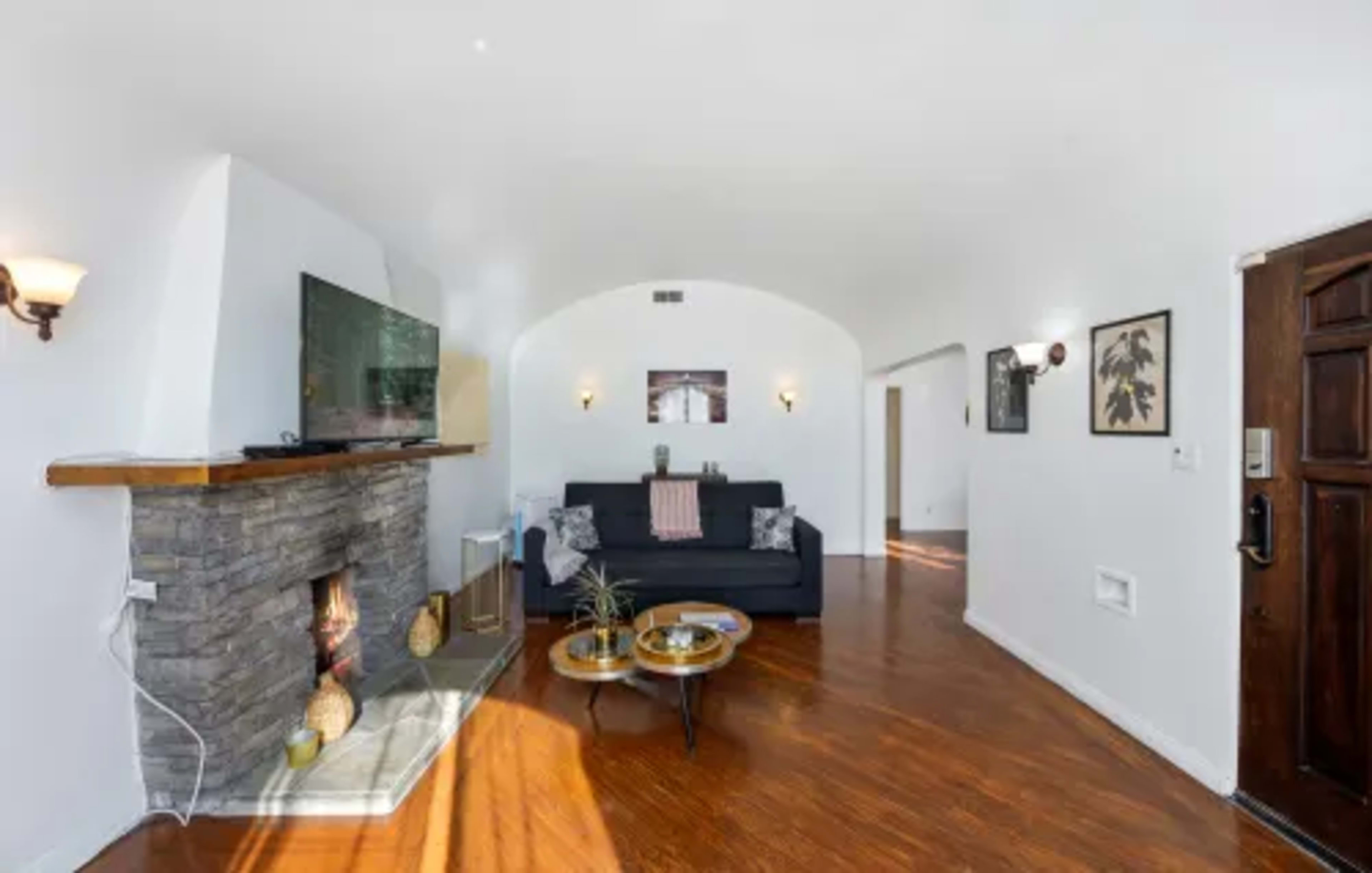 A modern living room featuring a stone fireplace, a black sofa, and decorative wall art.