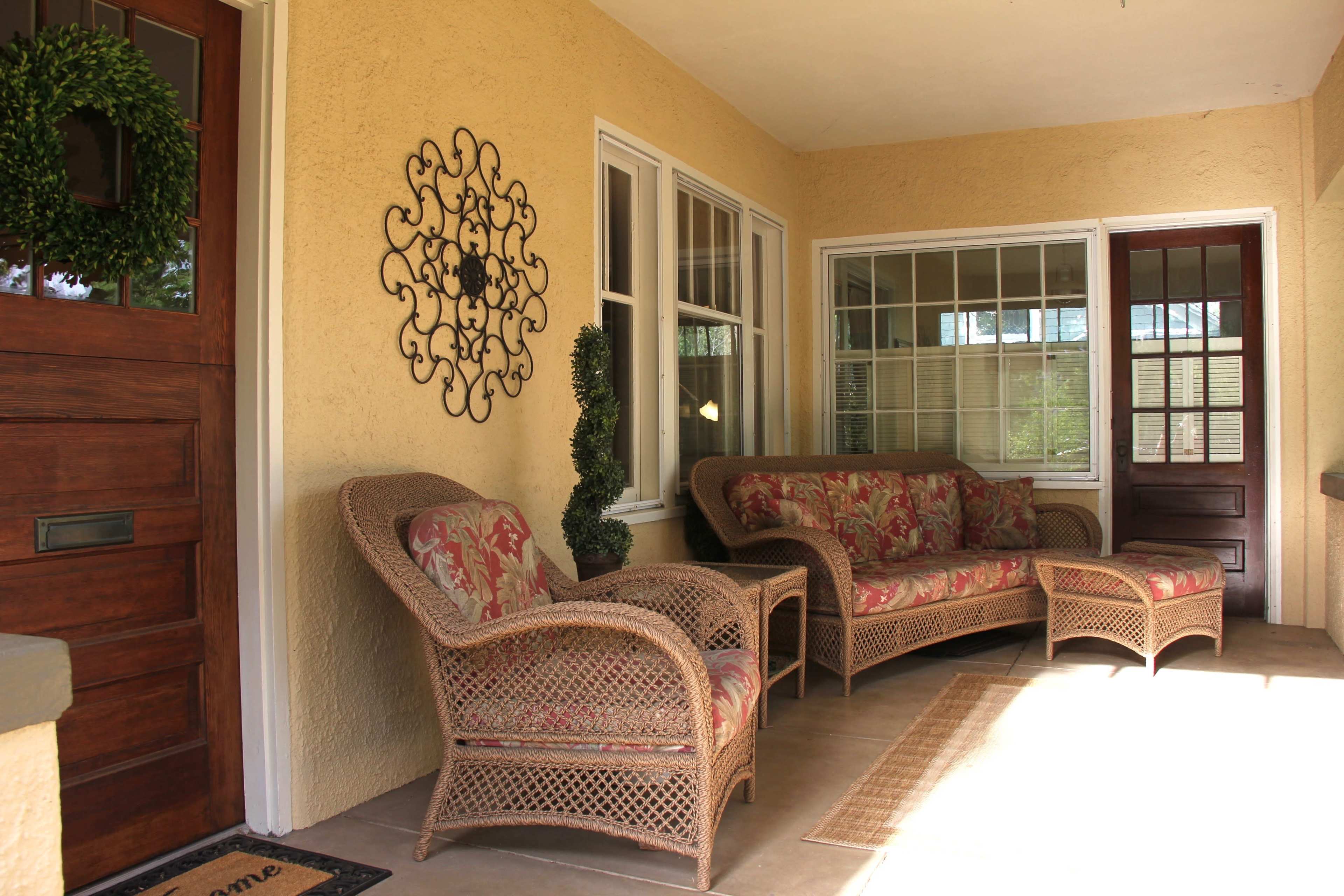 A porch area with a wicker seating arrangement, a decorative wall piece, and a wooden front door.