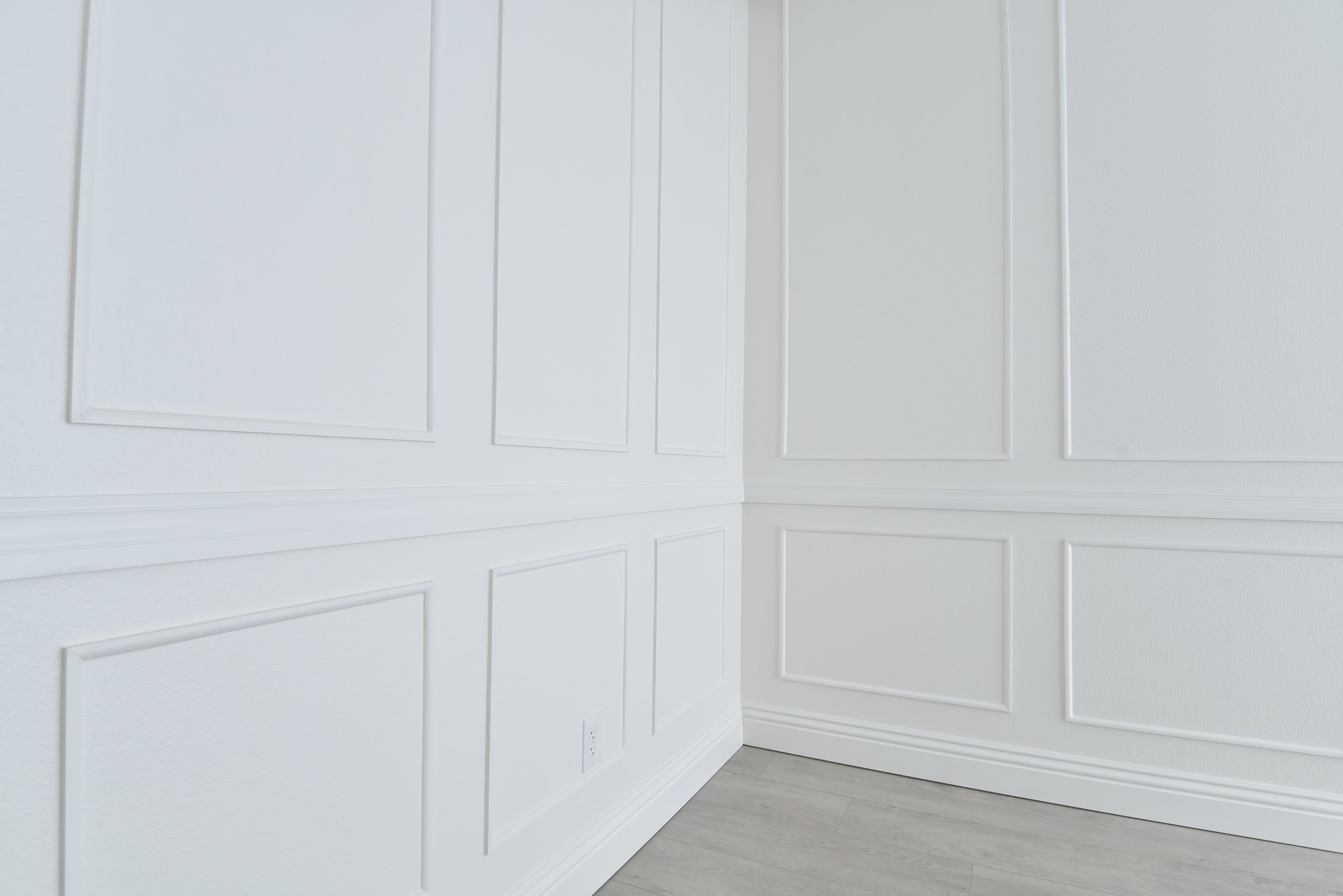 The image shows a corner of a room with white paneled walls and light gray flooring.
