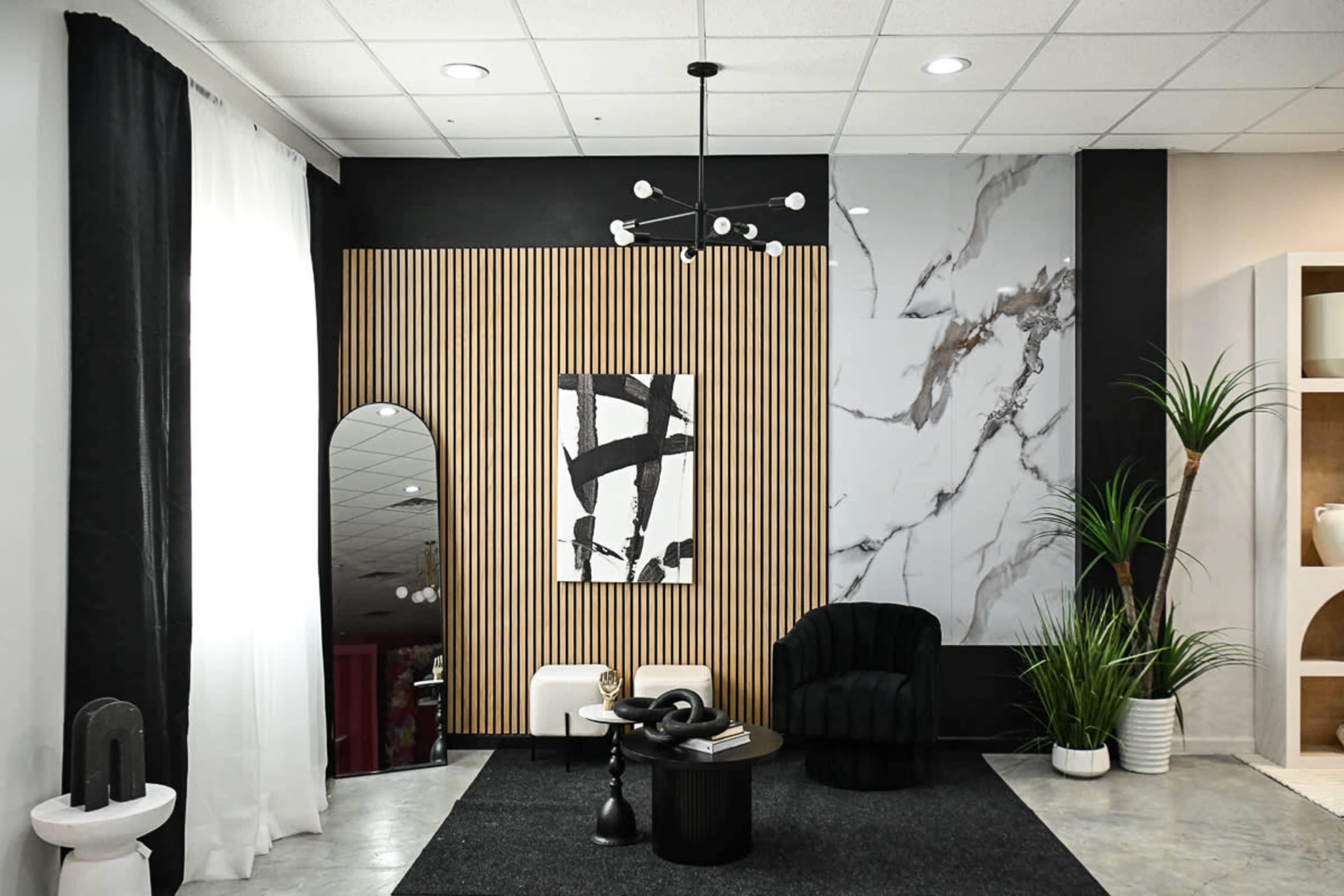 A modern interior space with a black wall, a marbled feature wall, wooden paneling, a round mirror, a black accent chair, and decorative plants.