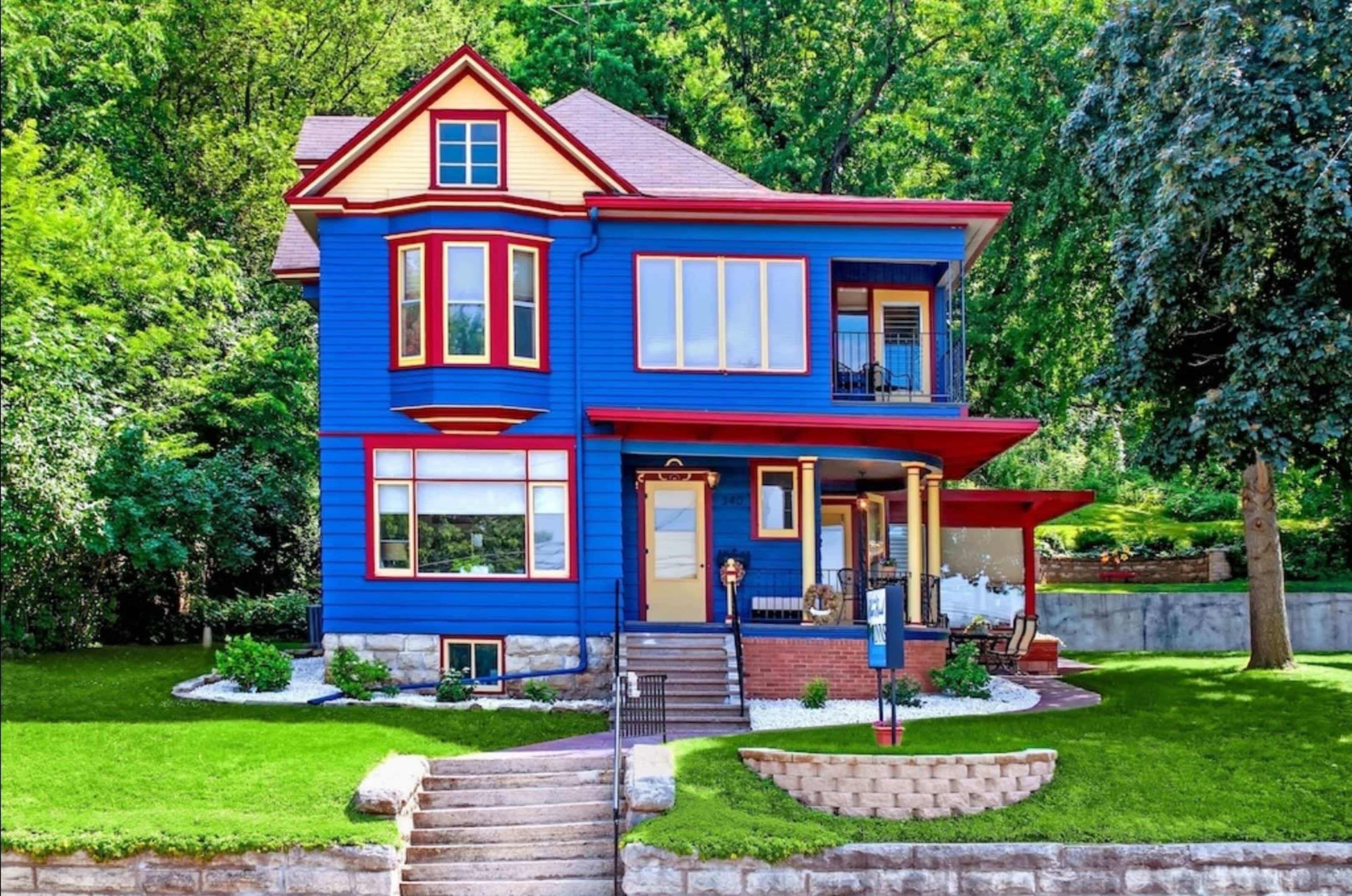 A vibrant blue Victorian-style house with red and yellow trim, surrounded by a well-maintained lawn and landscaping features.