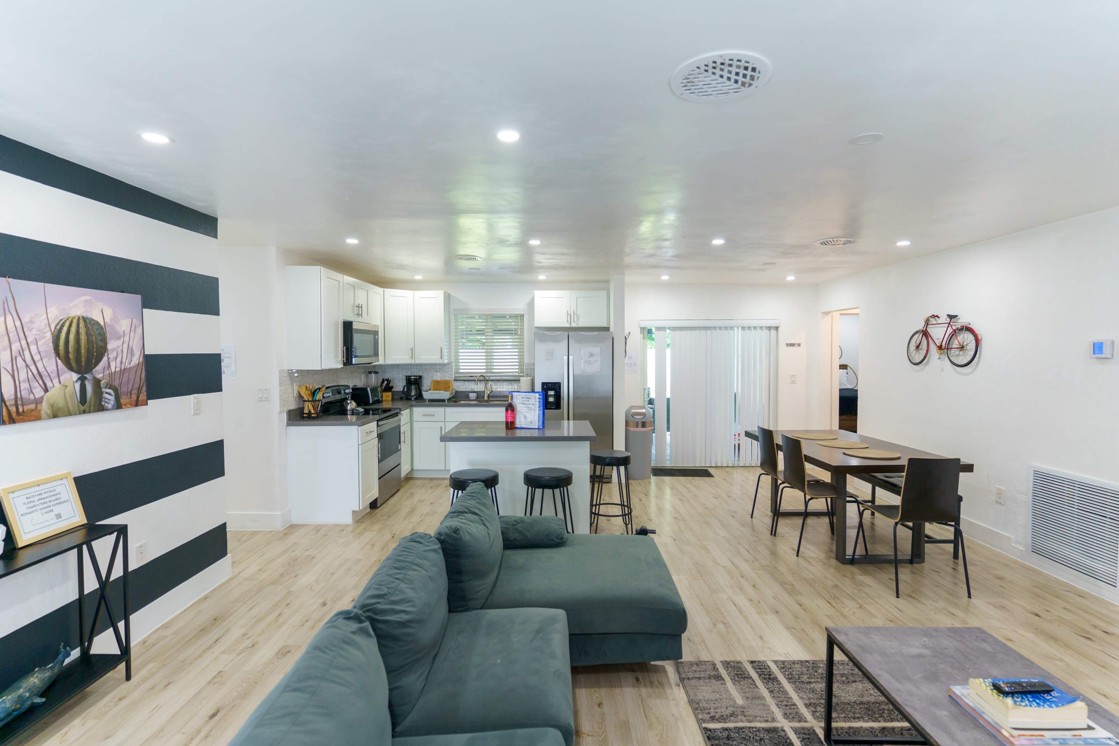 A modern, open-concept living space featuring a kitchen, dining area, and seating area with green couches.