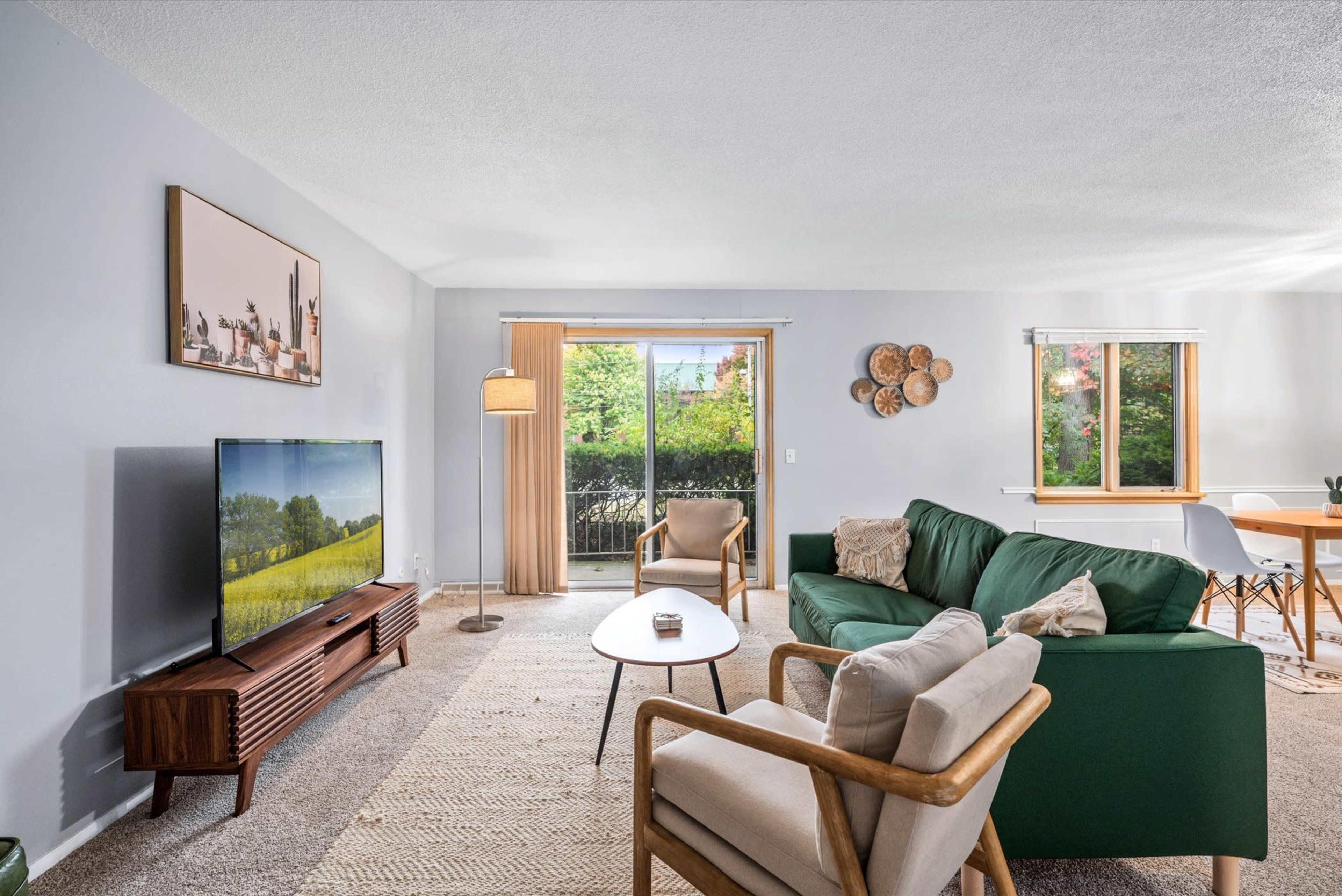 A living room with a television, green sofas, a wooden table, and a sliding door leading to a patio.