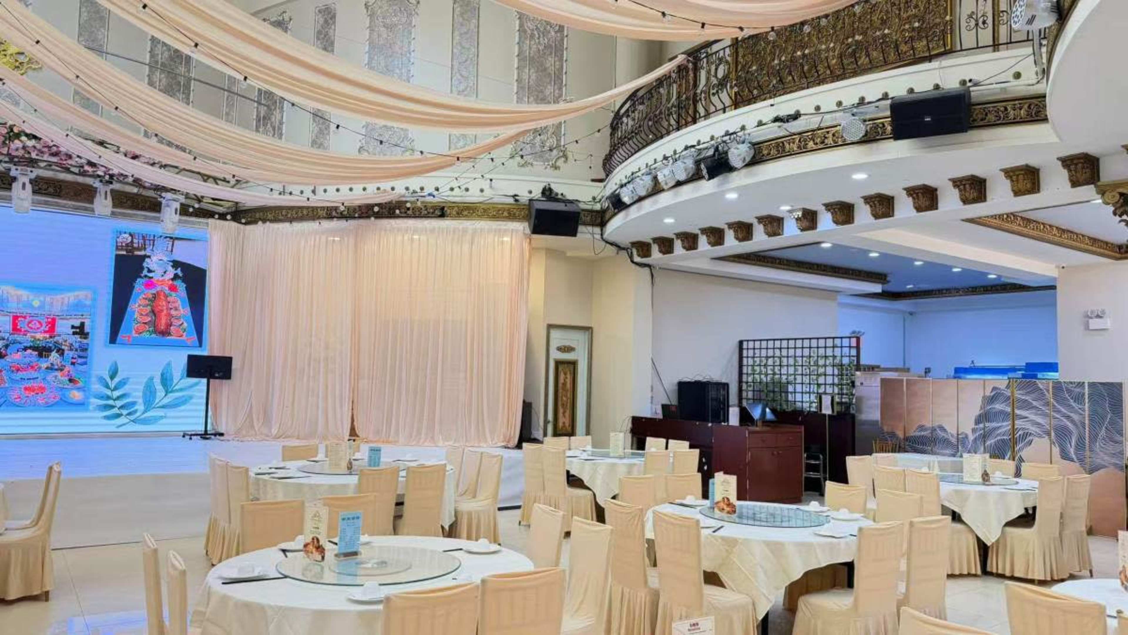 The image shows a large banquet hall with round tables set for dining, draped fabric ceilings, and a stage area in the background.