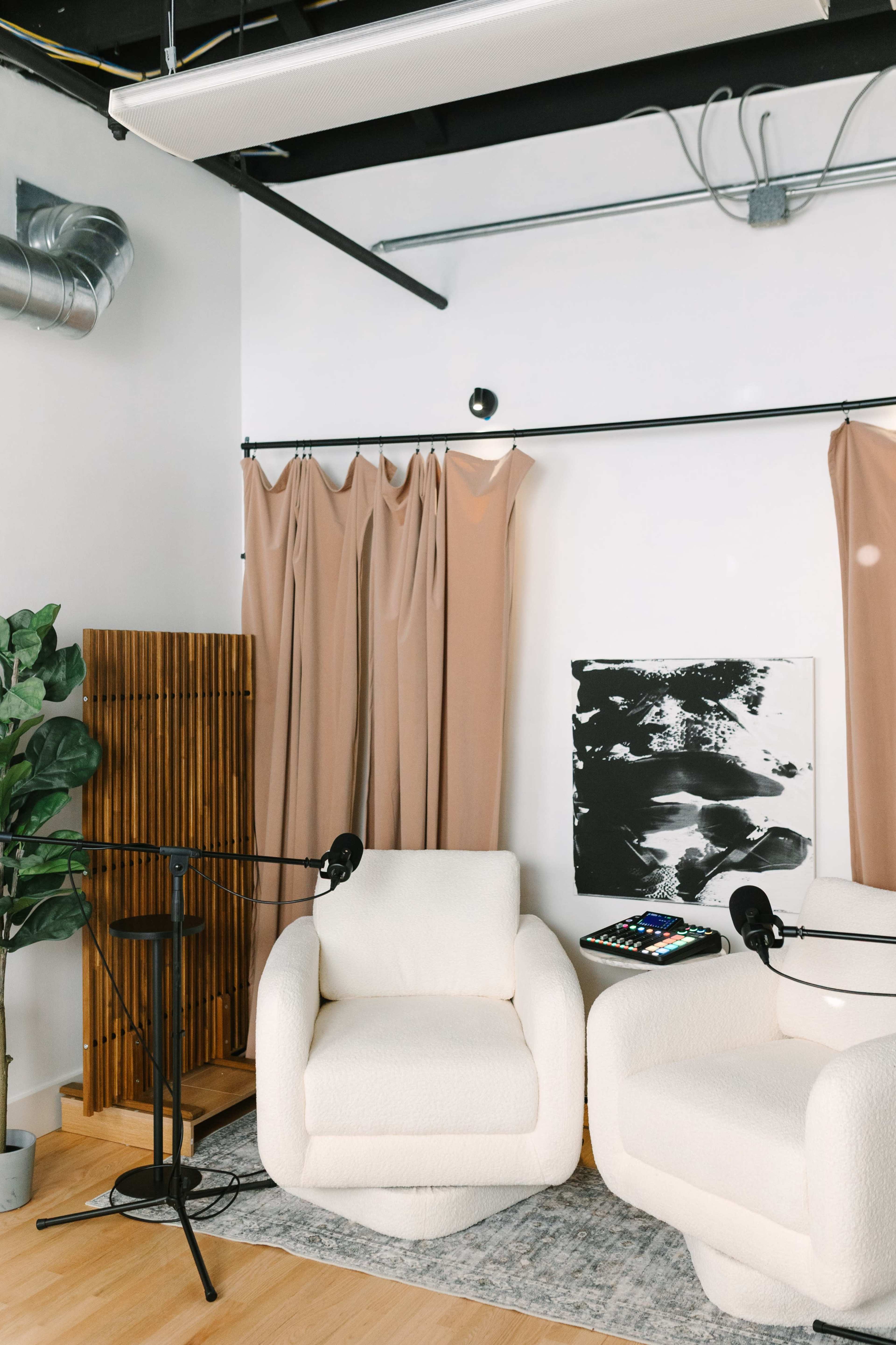 The image shows a modern podcast studio featuring two plush armchairs with microphones, draped curtains, and a decorative plant.