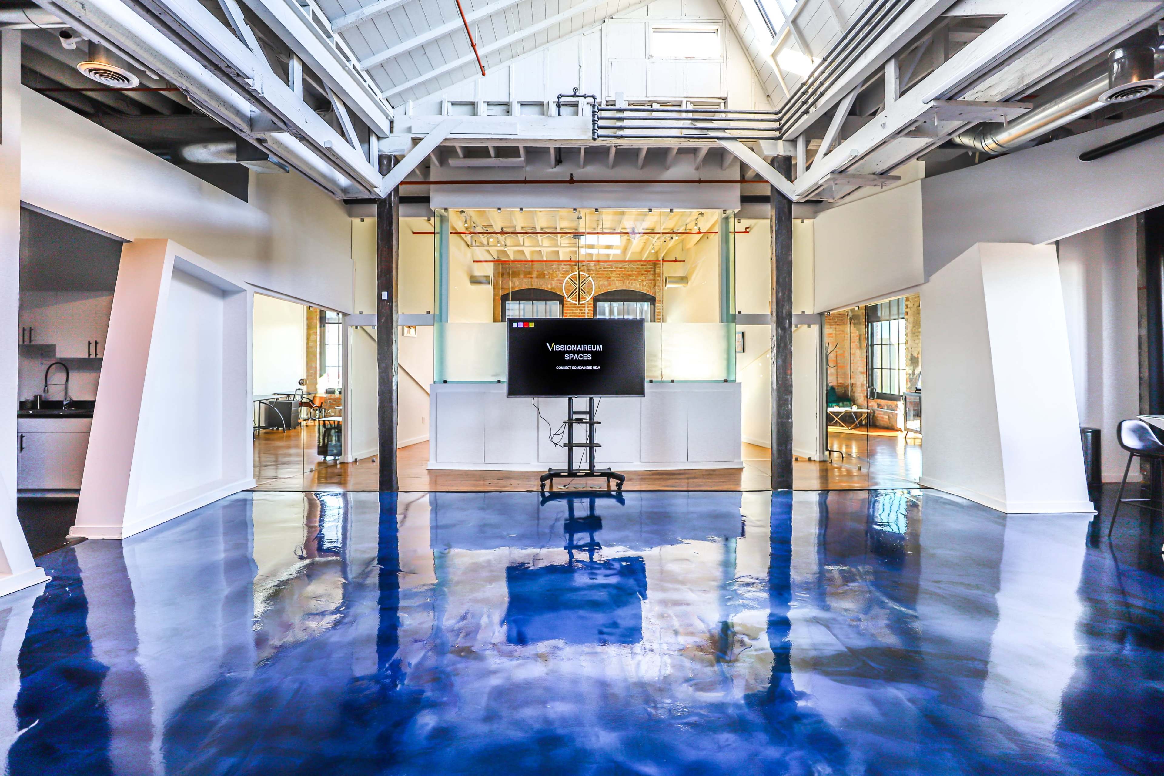 A spacious, industrial-style interior with polished blue flooring and a television mounted on a stand in a well-lit area.