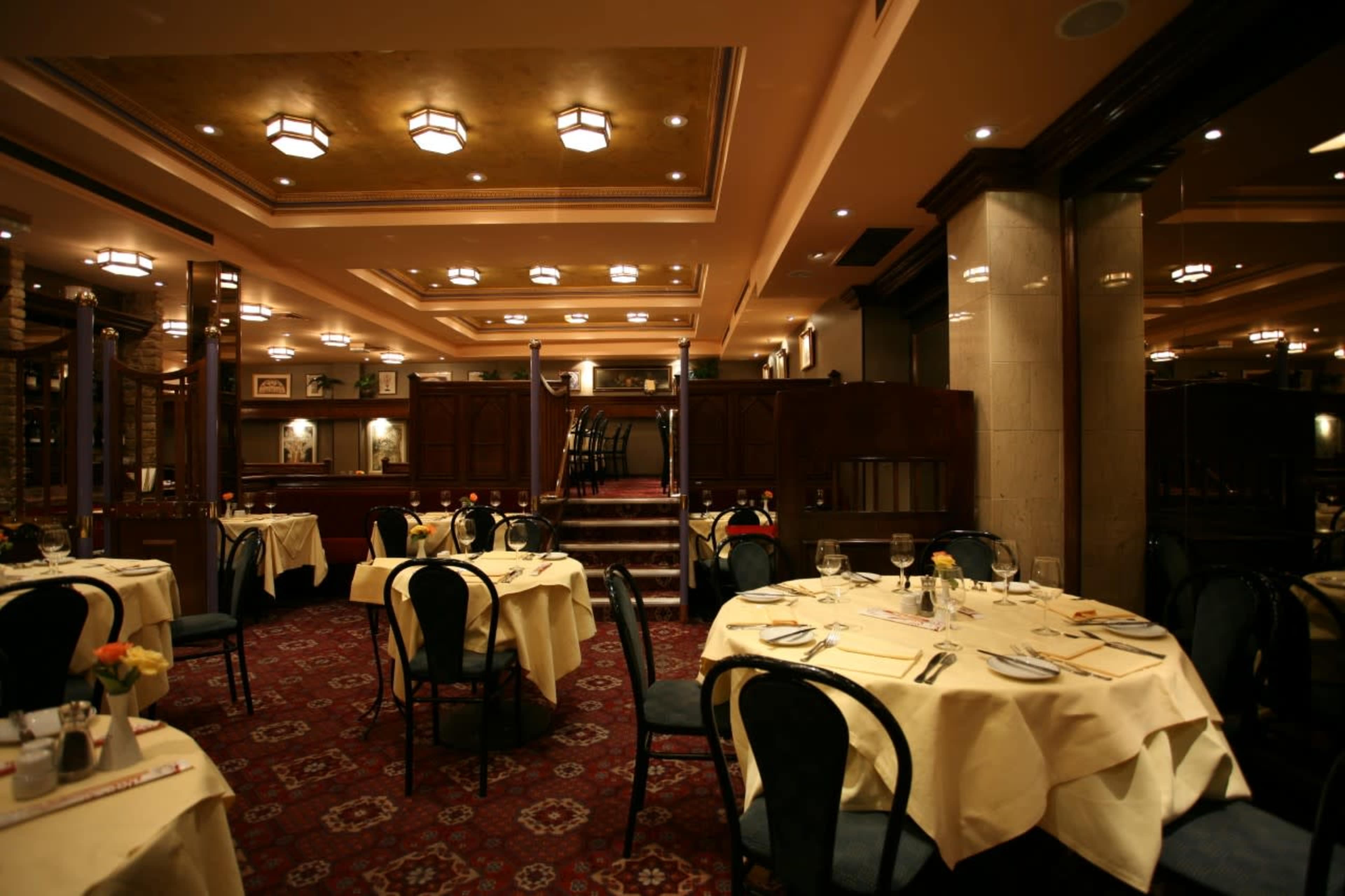 An elegantly designed restaurant interior with round tables covered in cream-colored tablecloths and ornate light fixtures on the ceiling.