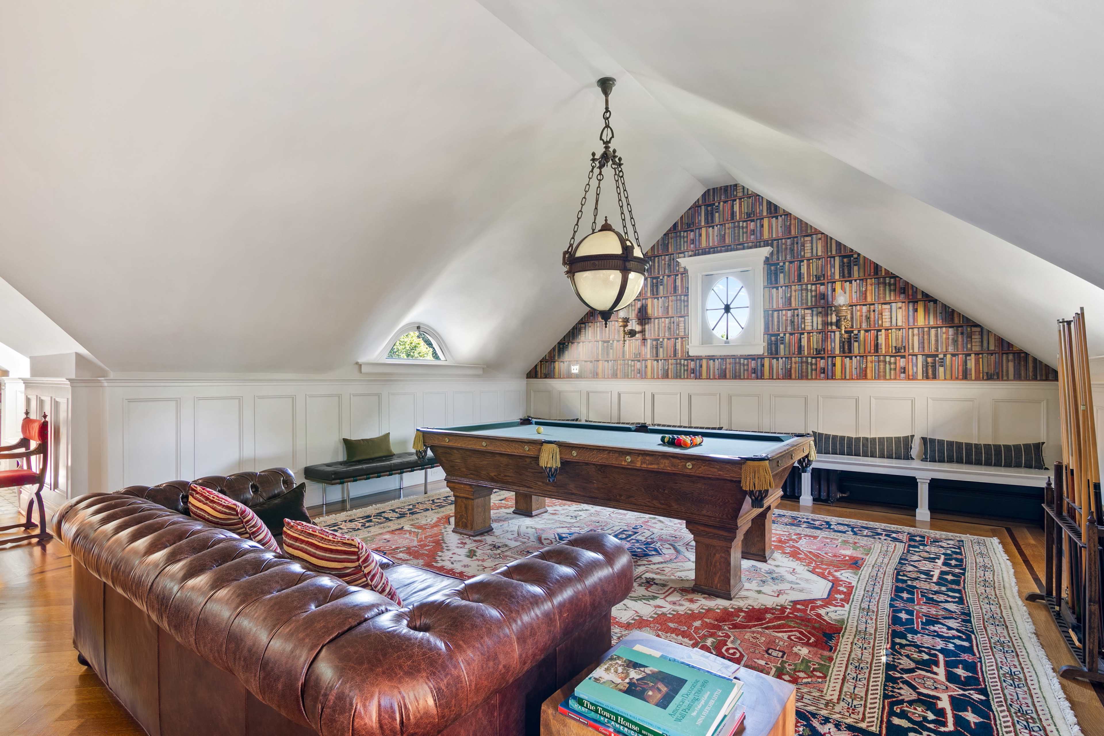 The room features a pool table surrounded by a leather couch and a wall adorned with a patterned bookshelf backdrop.