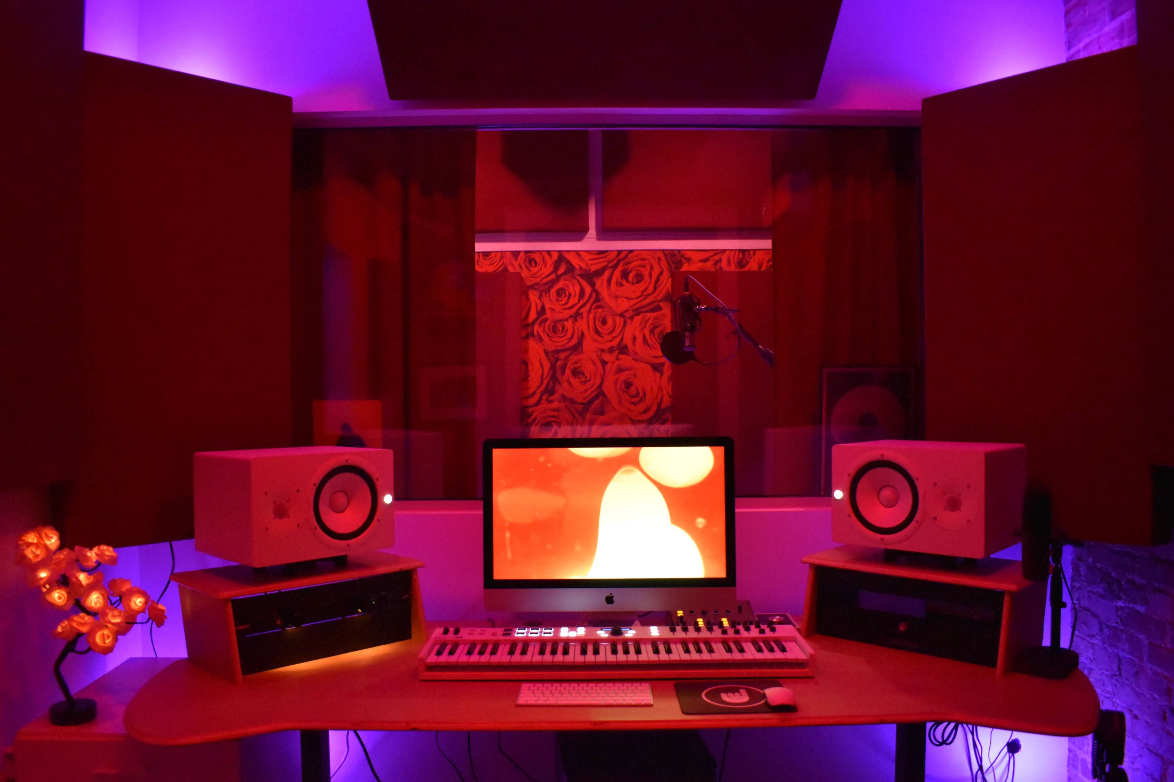 A music studio setup with a computer screen, keyboard, and speakers, surrounded by purple and red lighting.