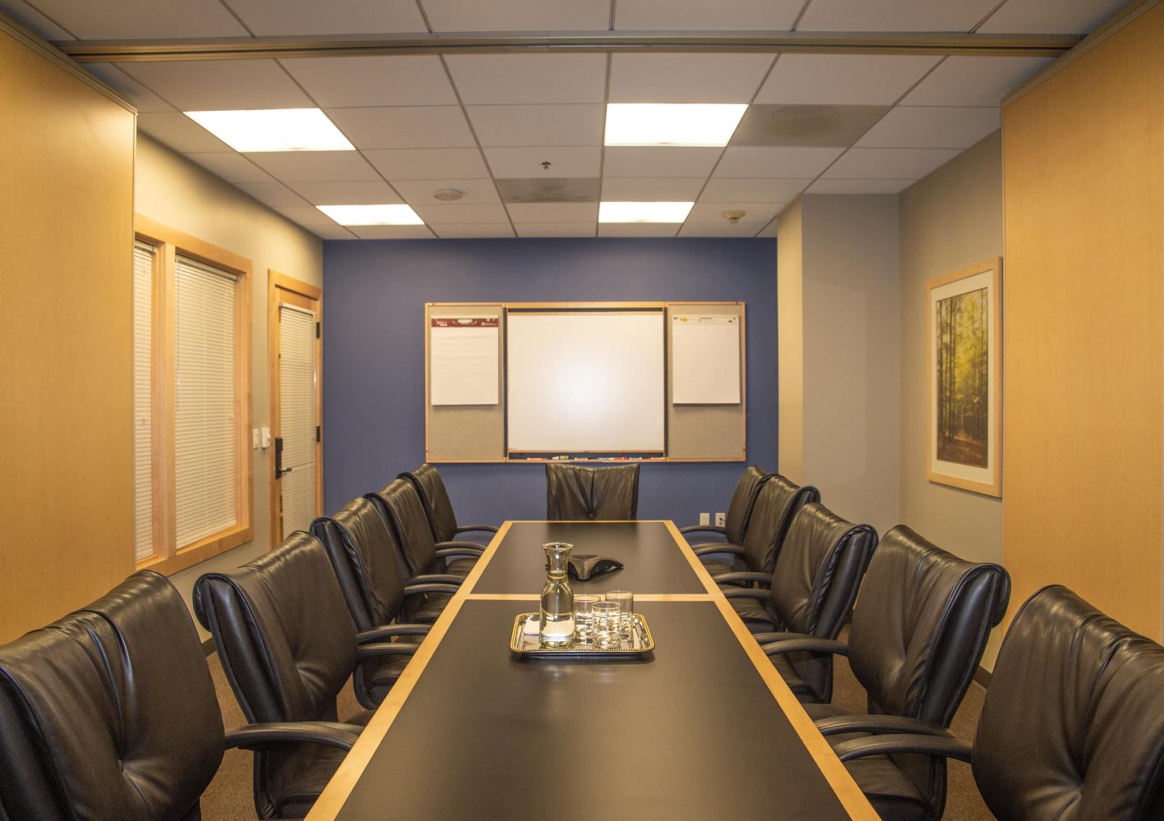 A conference room with a long table, ten black leather chairs, a whiteboard, and a presentation board mounted on the wall.