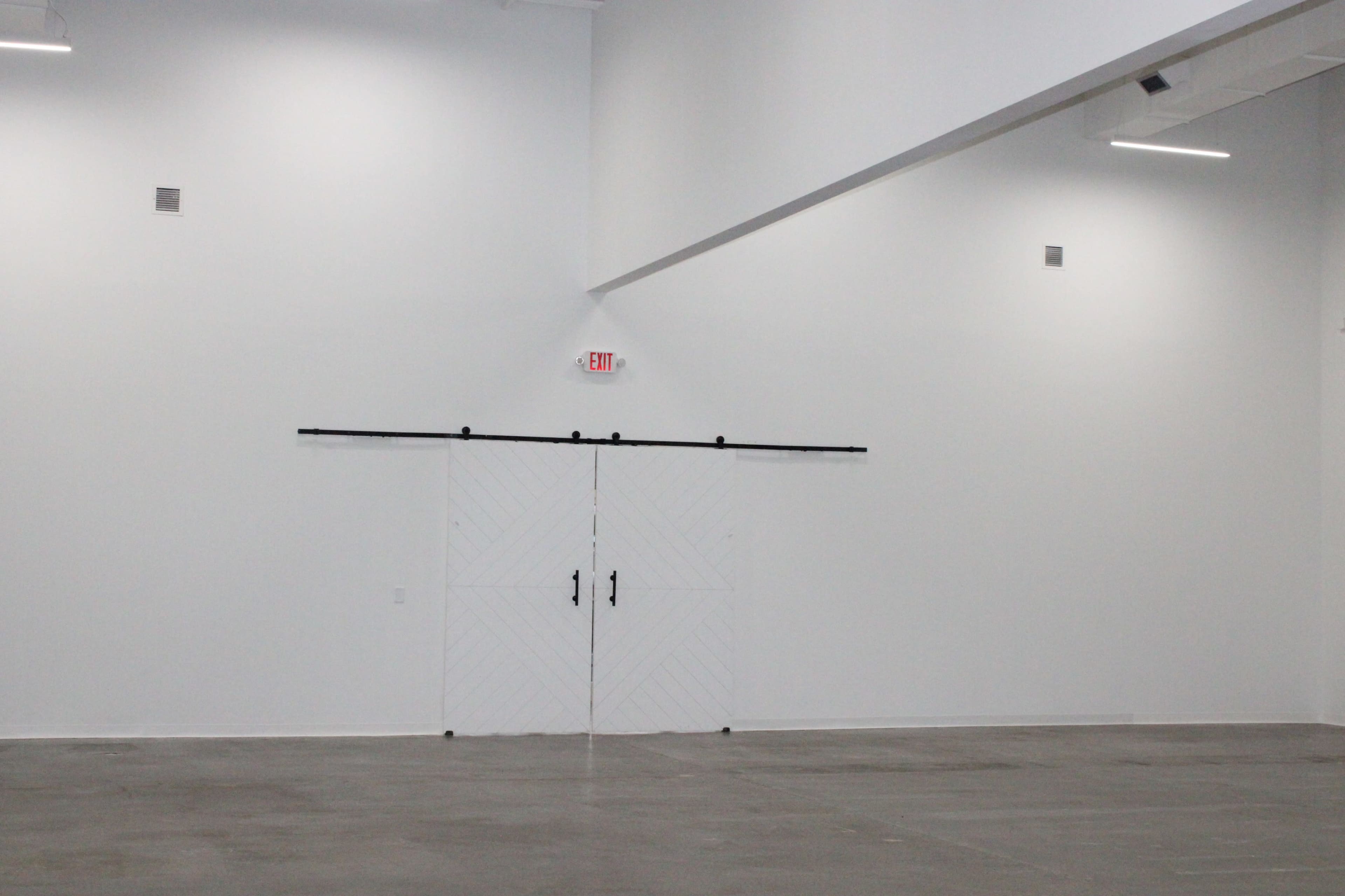 An empty room features a large double door on a sliding track against a plain white wall.