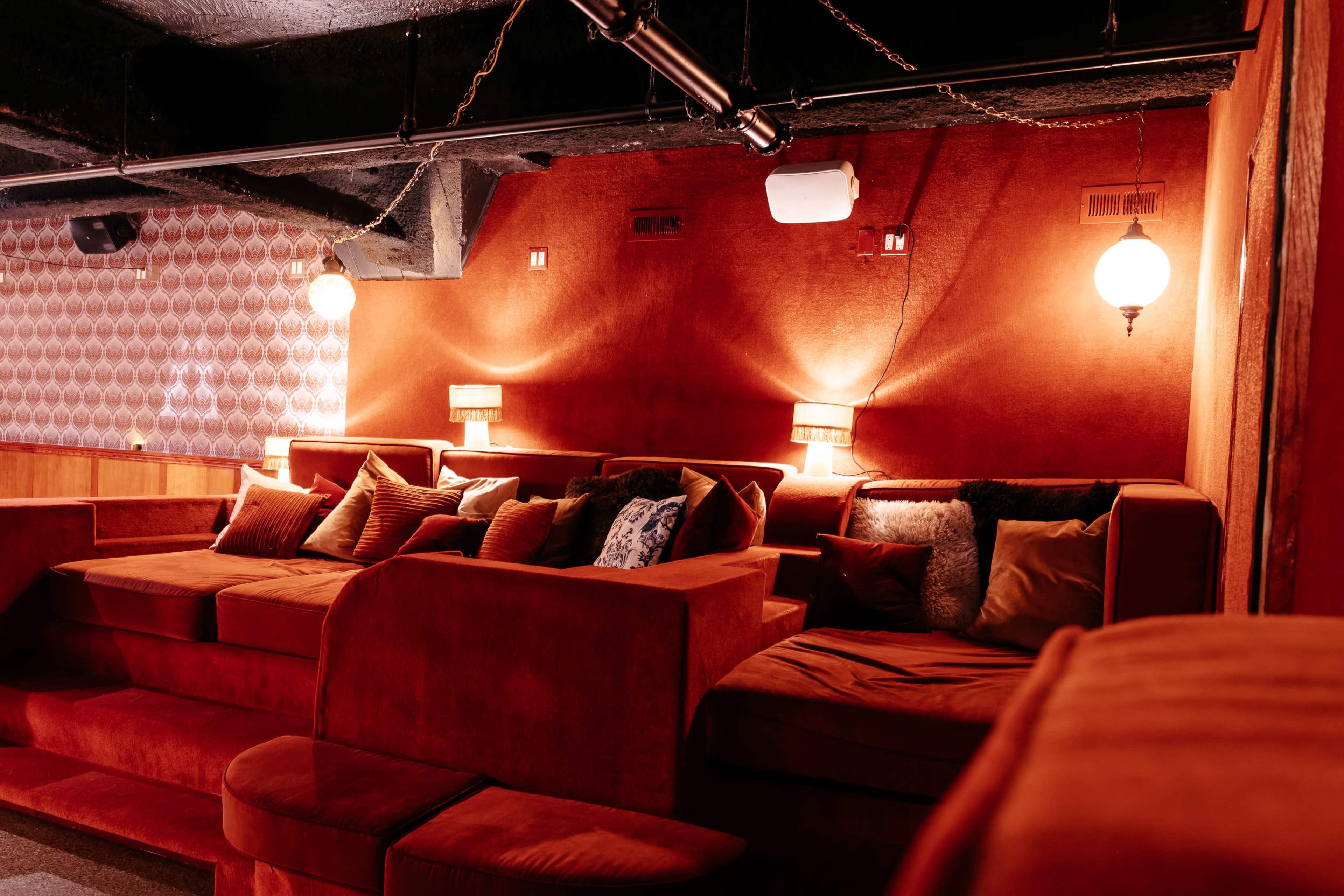 The scene features a cozy lounge area with plush red couches, warm lighting from wall sconces, and decorative pillows.