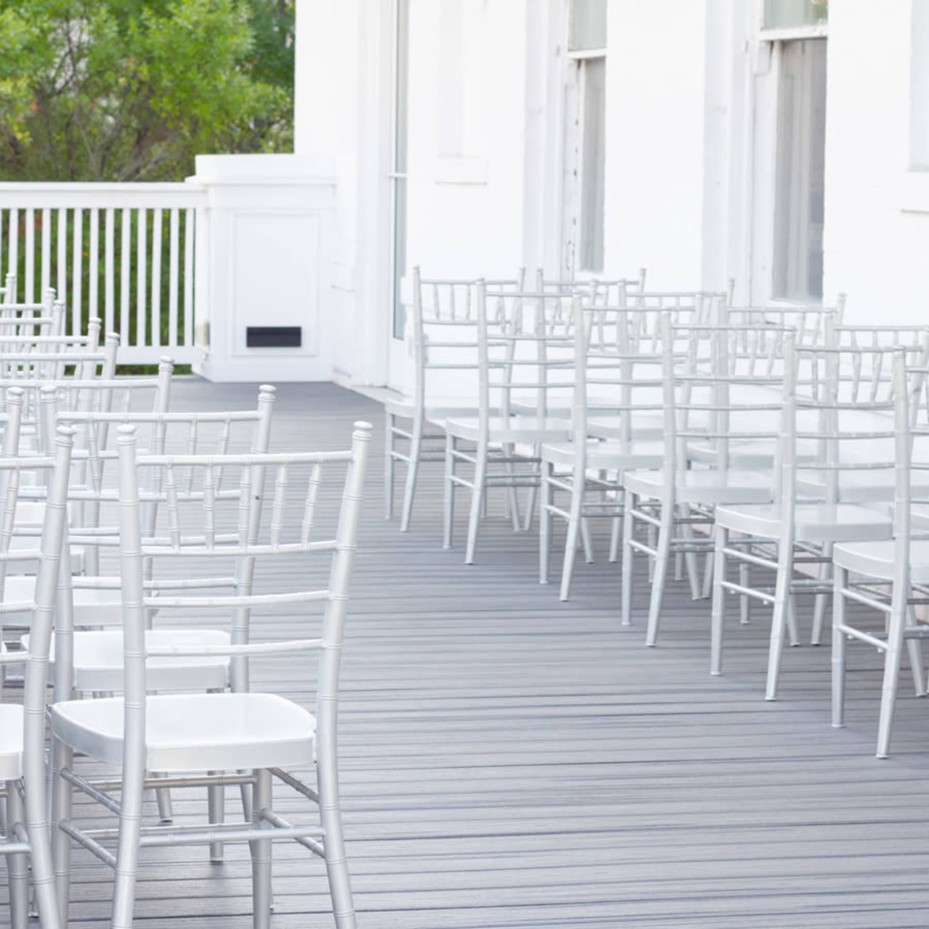 The image shows rows of silver chiavari chairs arranged on a wooden deck.