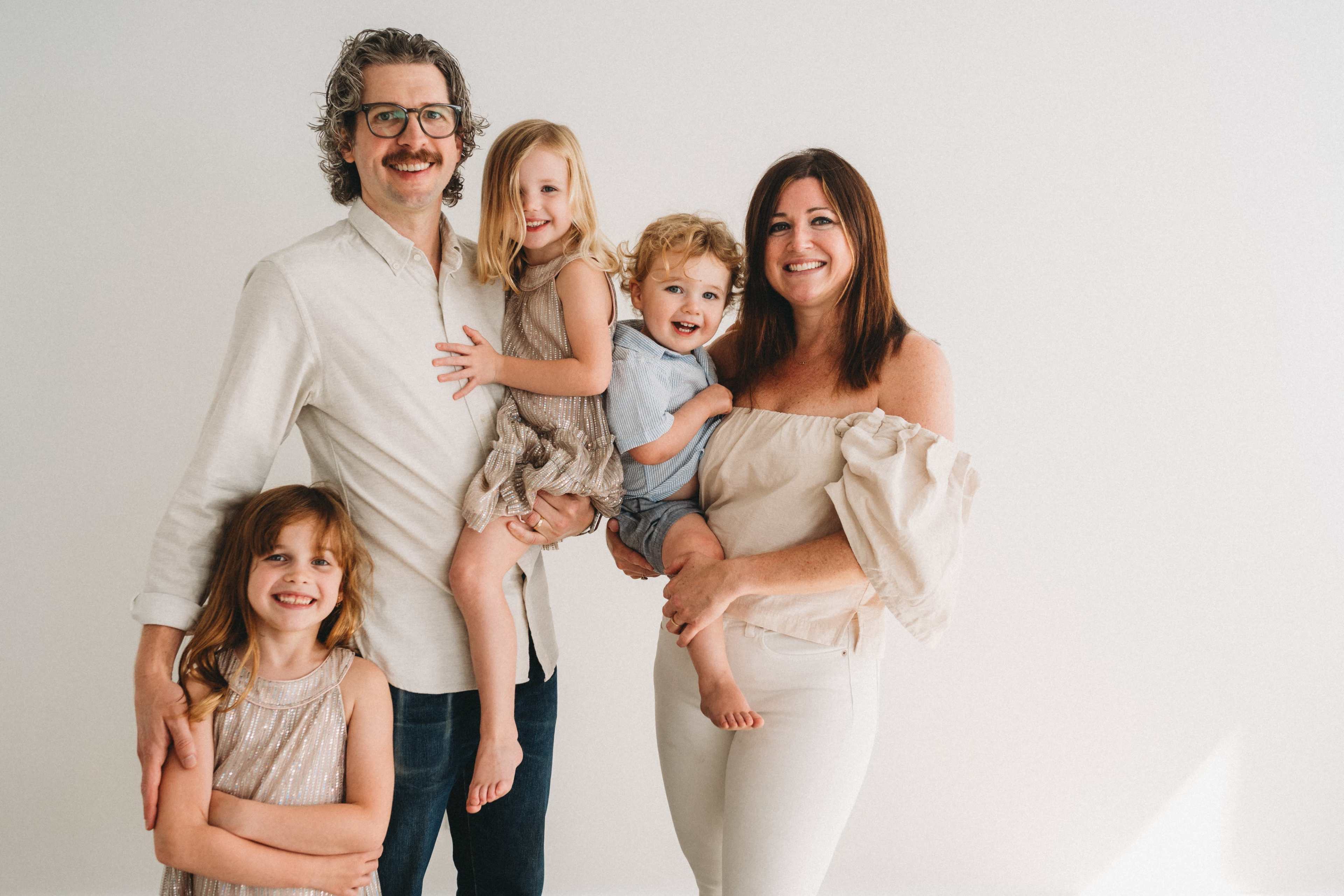 A family of four stands together, with the parents holding two young children, and the third child beside them.