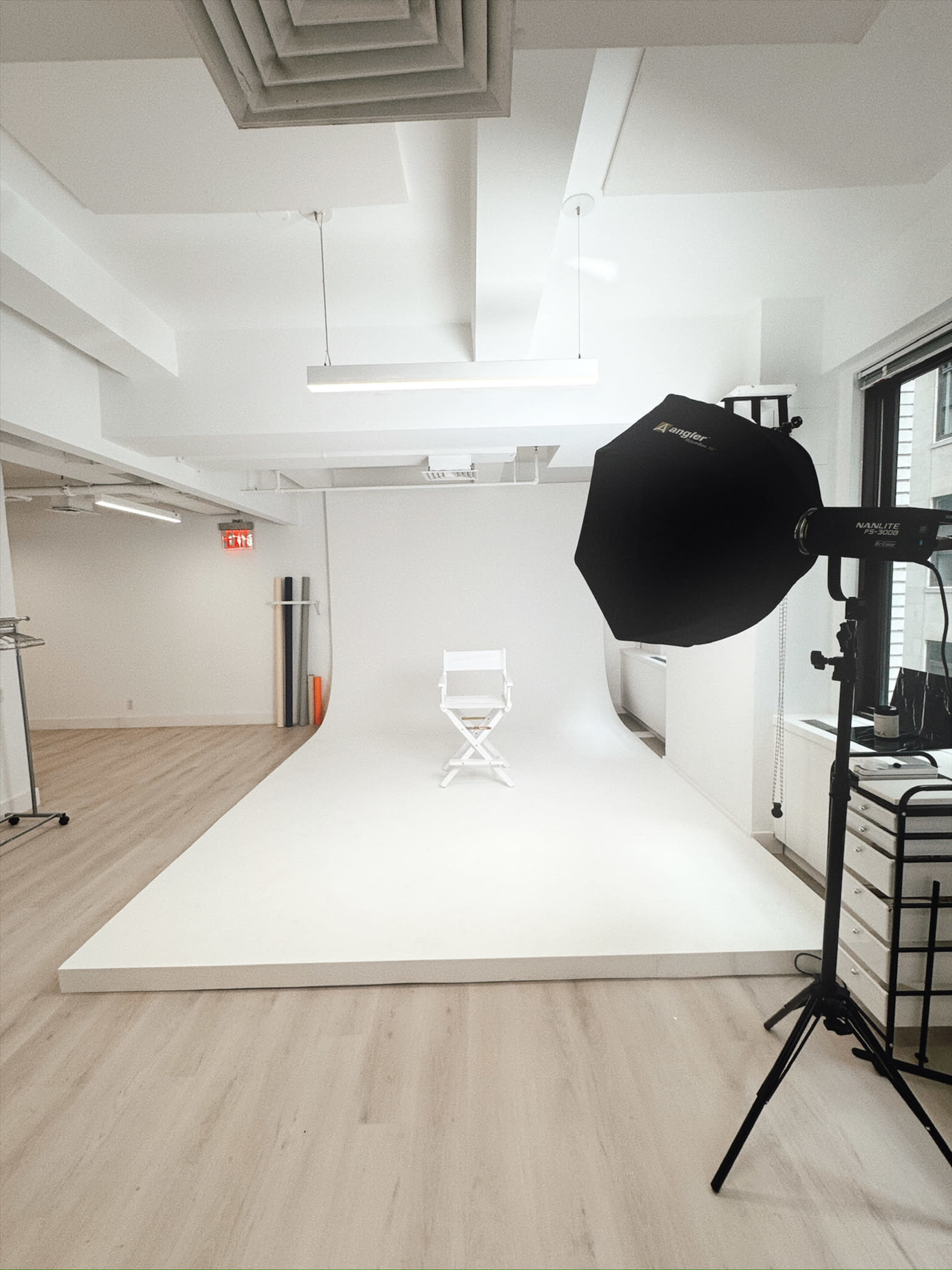 A brightly lit photography studio features a white backdrop, a director's chair, and studio lighting equipment.