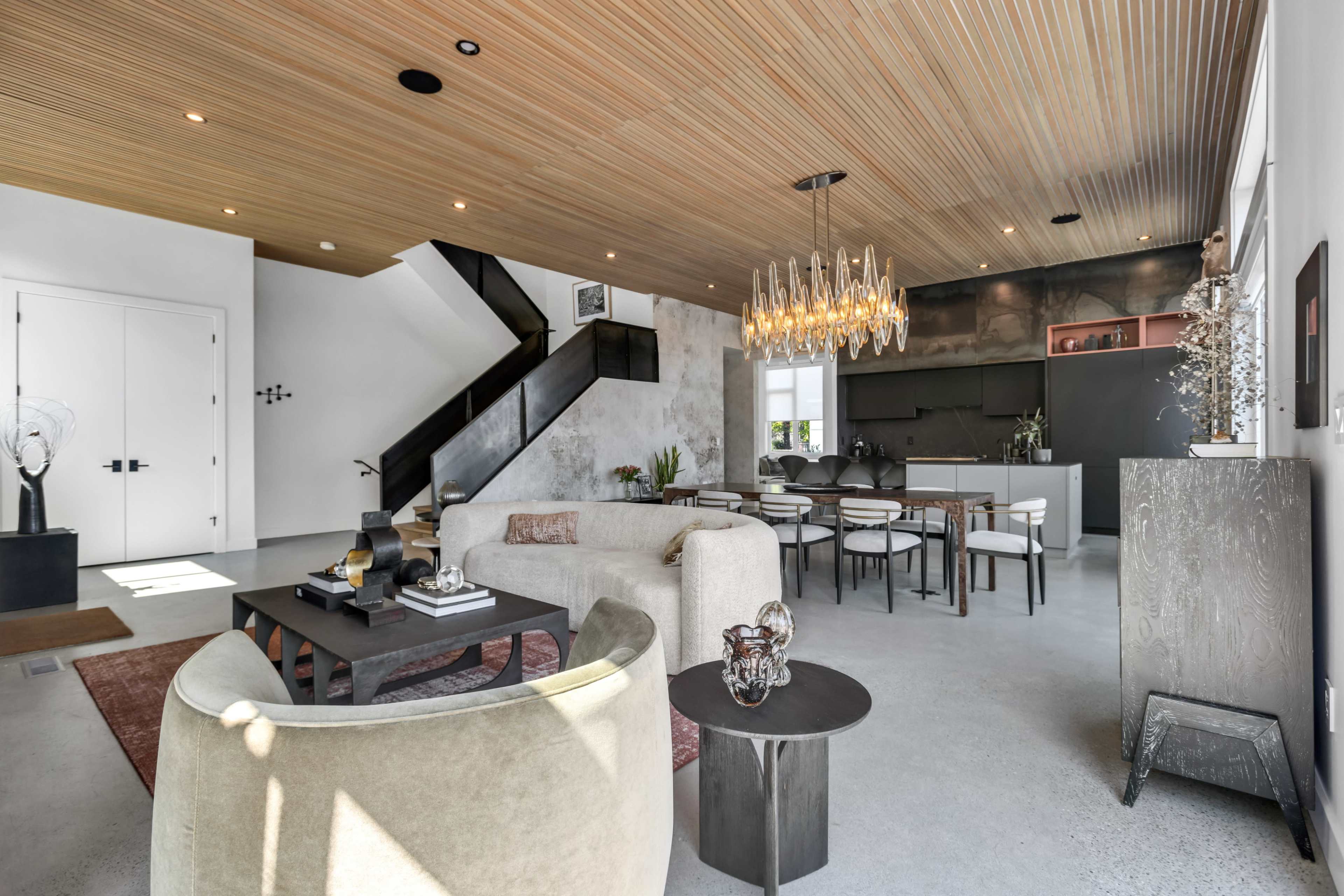 The image shows a modern open-concept living area featuring a light-colored sofa, a dining table with chairs, and a sleek kitchen in the background.