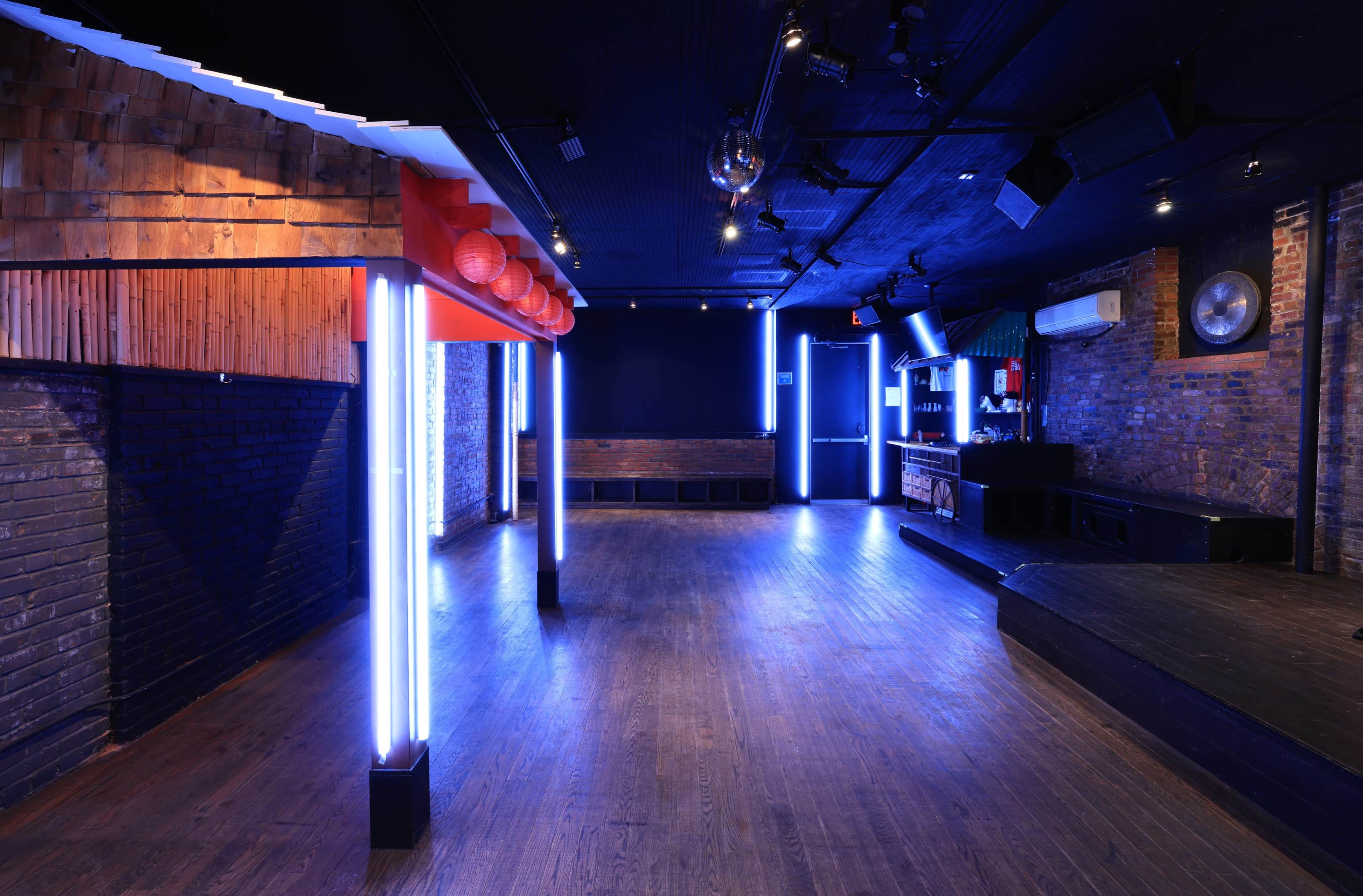 An empty music venue with wooden floors, exposed brick walls, and blue neon lighting along the columns.