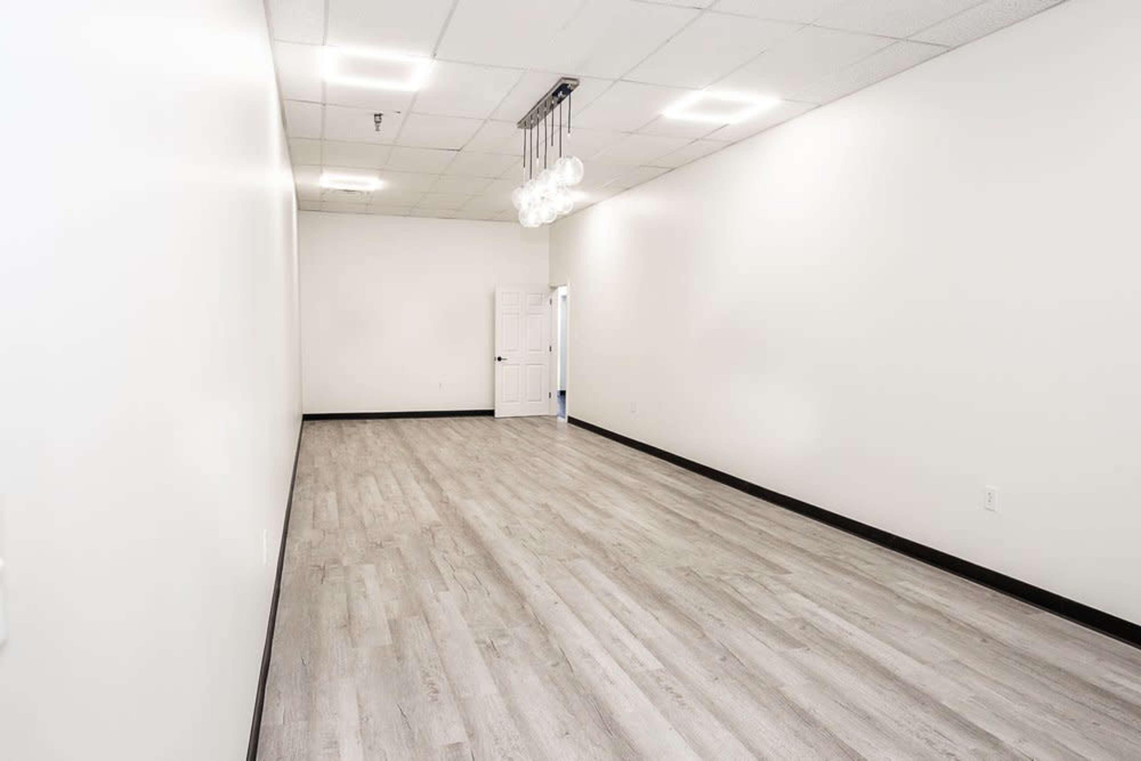 A spacious, empty room with light-colored walls and flooring, featuring a few pendant lights suspended from the ceiling.