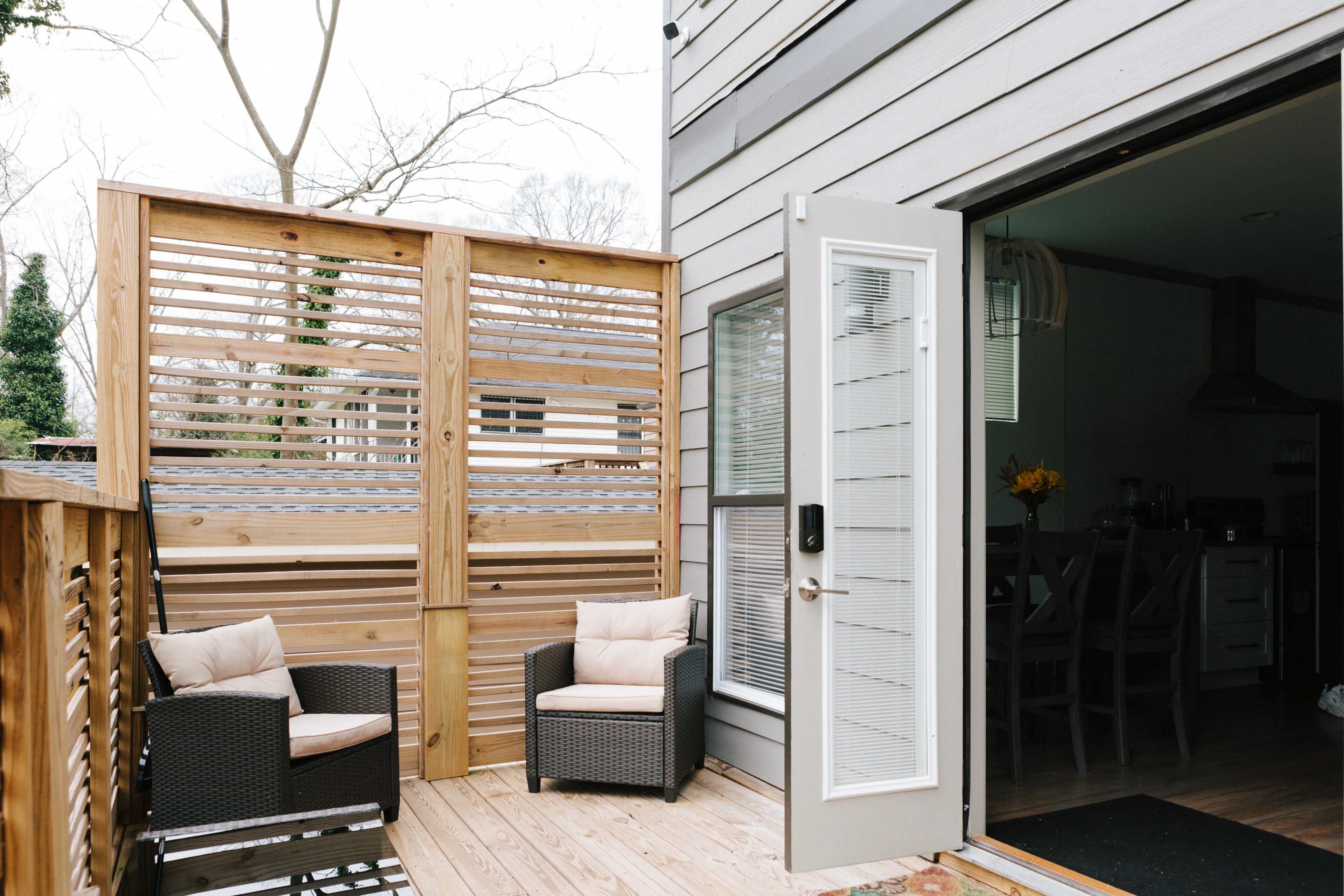 A wooden deck features two chairs and a sliding door leading into a house, with a slatted wooden fence providing some privacy.