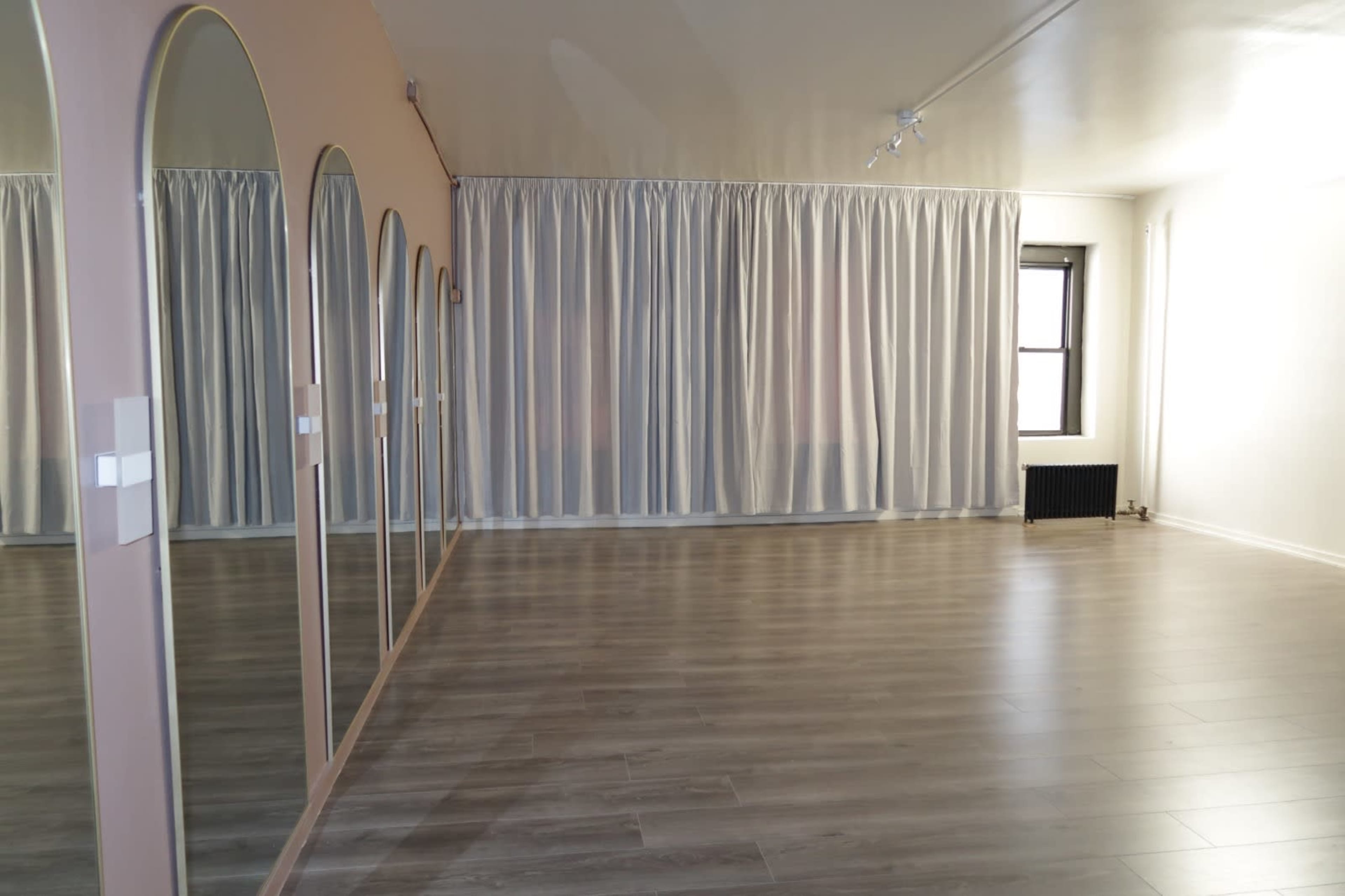 The image shows a spacious room with large mirrors on one wall and light-colored curtains covering the windows.