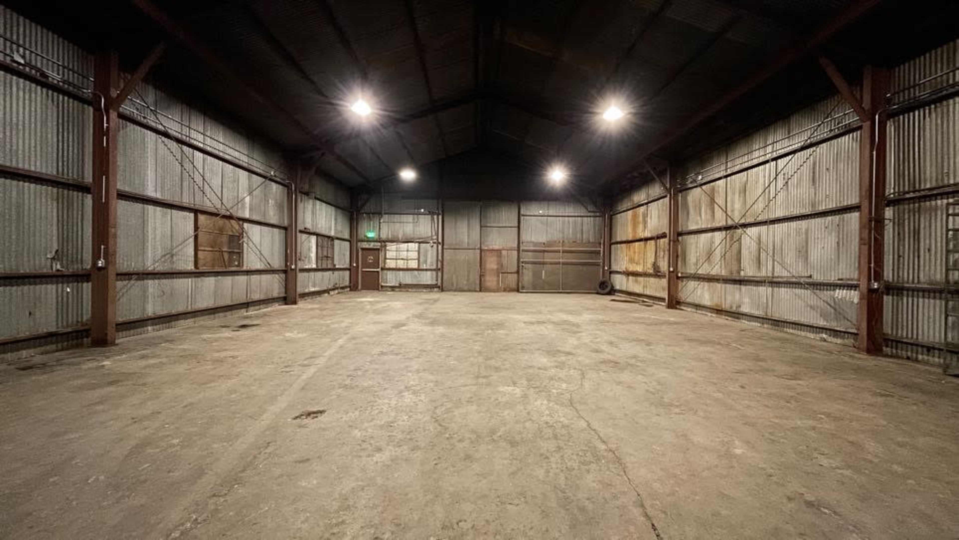 The interior of a large, empty warehouse with exposed metal walls and a concrete floor.