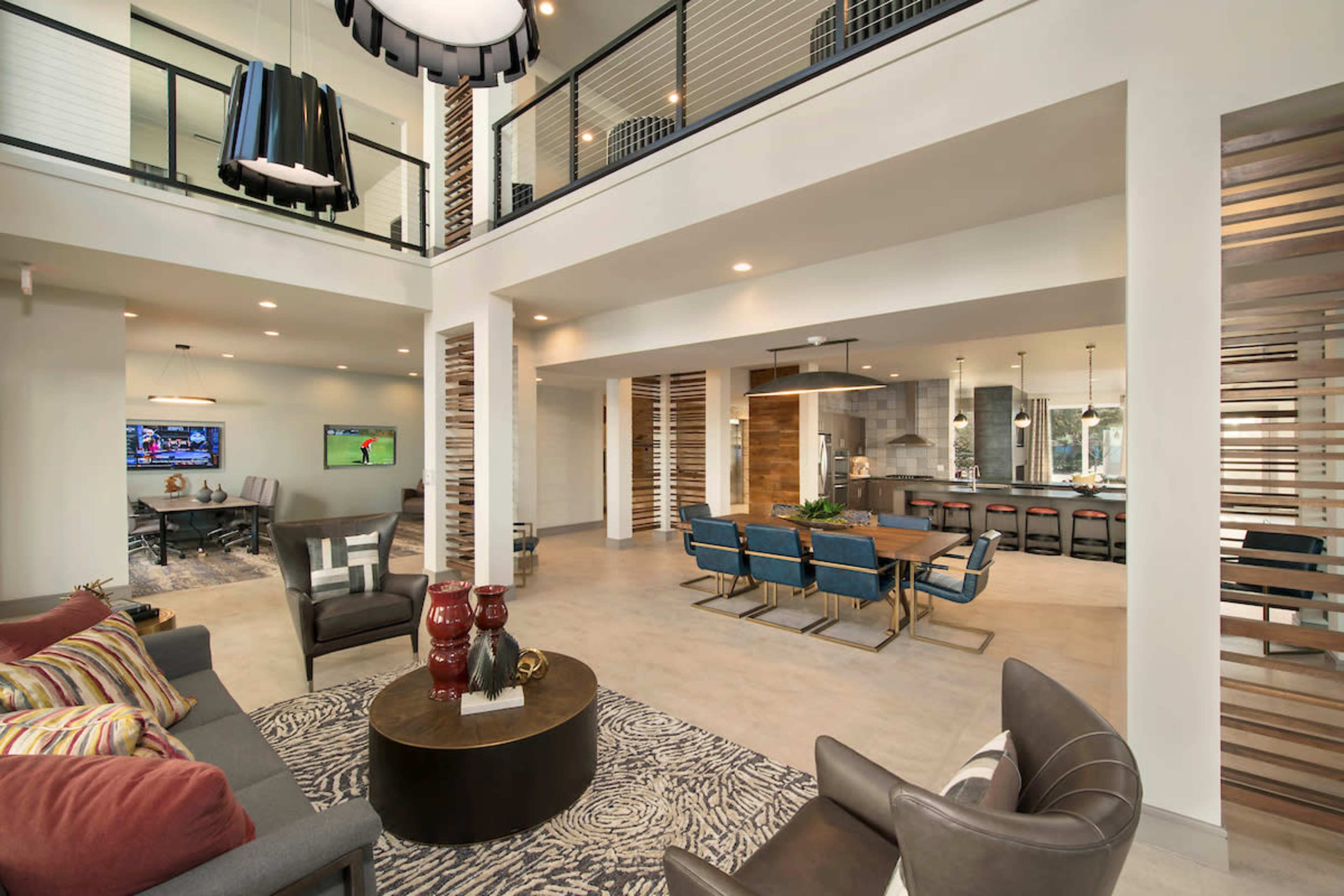 A modern open-plan living area featuring a seating space with a gray sofa, a round coffee table, and a dining area with blue chairs and a large table.