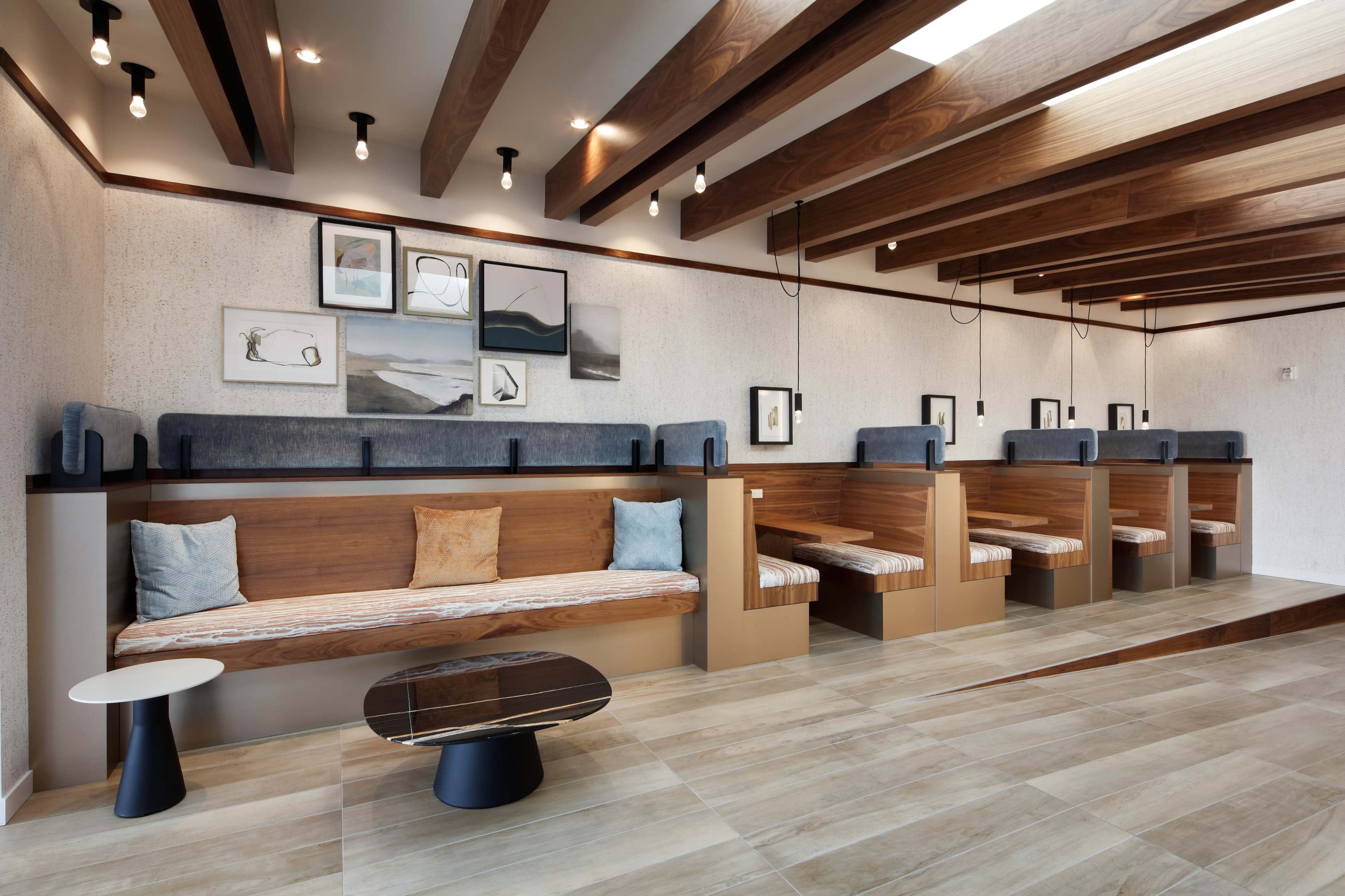 A modern interior space featuring wooden beams, seating areas with cushions, and framed artwork on the walls.