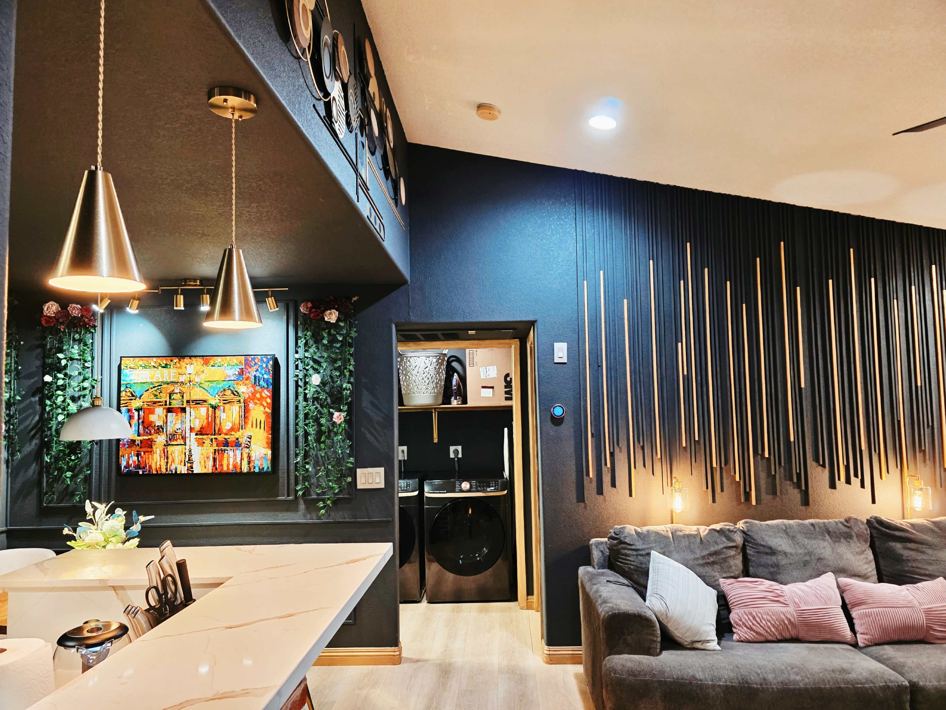 The image shows a modern living space featuring a cozy sofa, decorative wall art, and an entrance to a laundry area with sleek lighting and stylish wall textures.