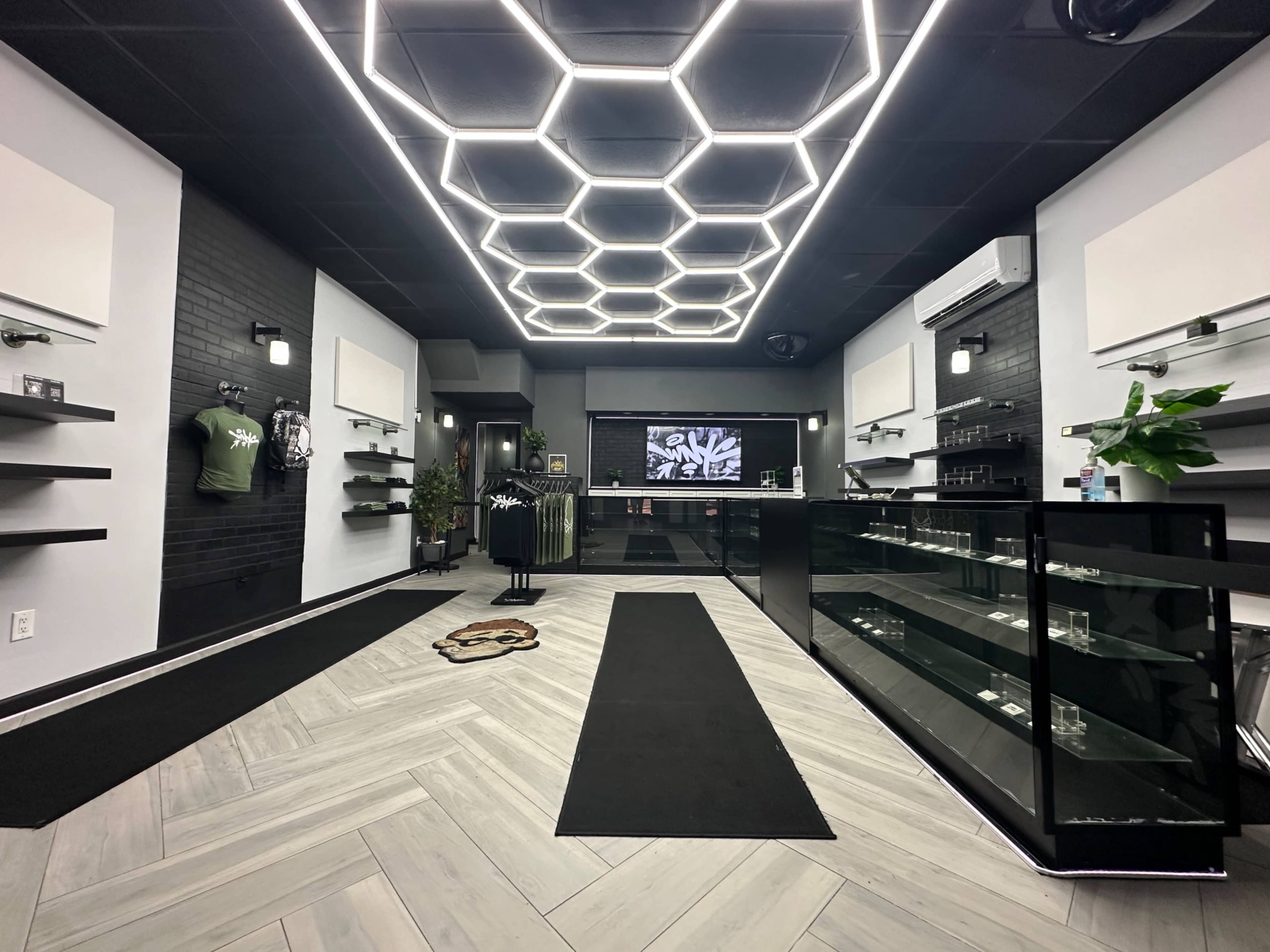 The image shows a modern retail space with a geometric ceiling design, featuring black walls, a glass display counter, and merchandise shelves along the sides.
