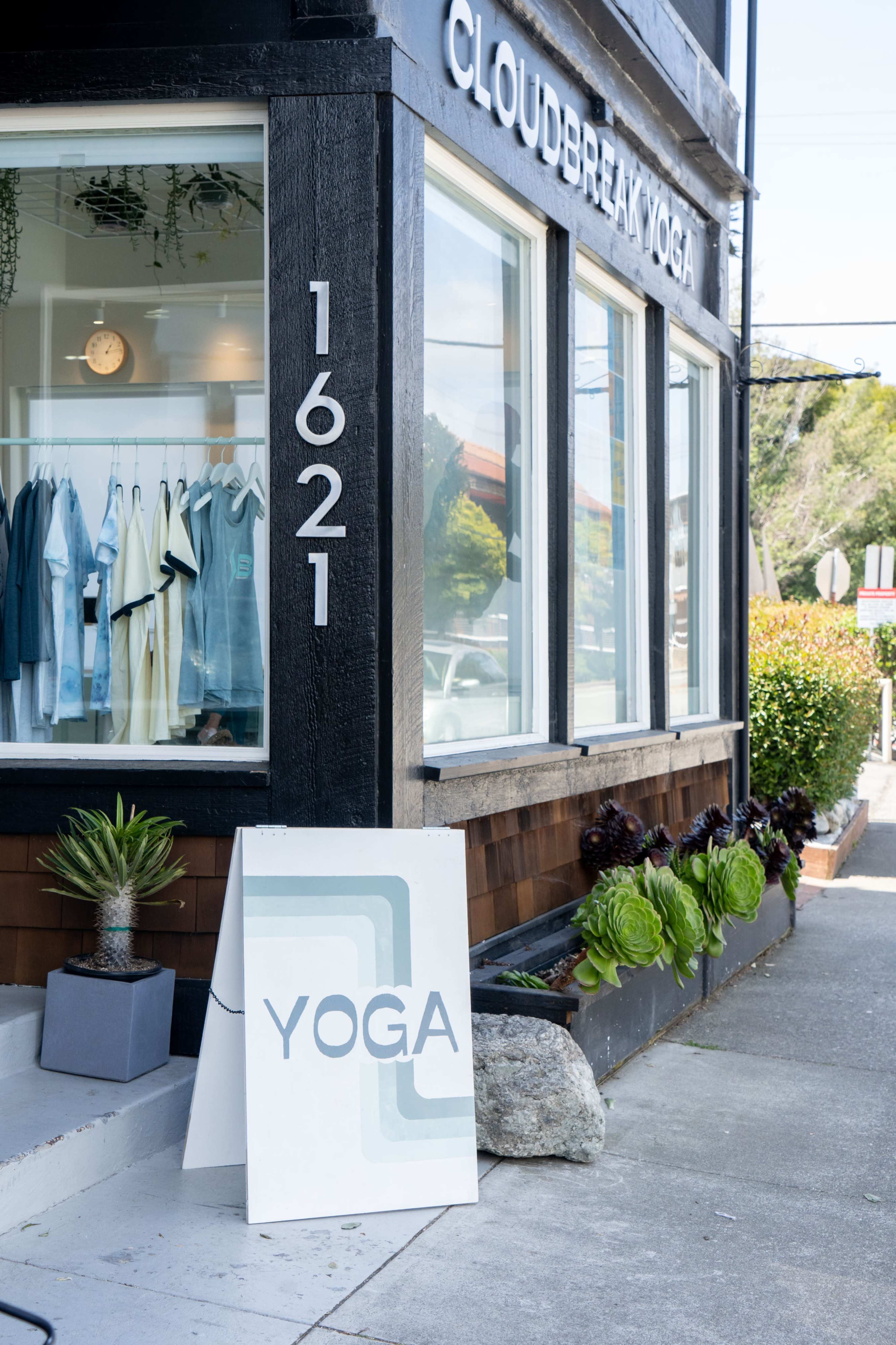The exterior of a yoga studio named "Cloudbreak Yoga," featuring a sign, a white A-frame board displaying "YOGA," and a storefront with clothing displayed in the window.
