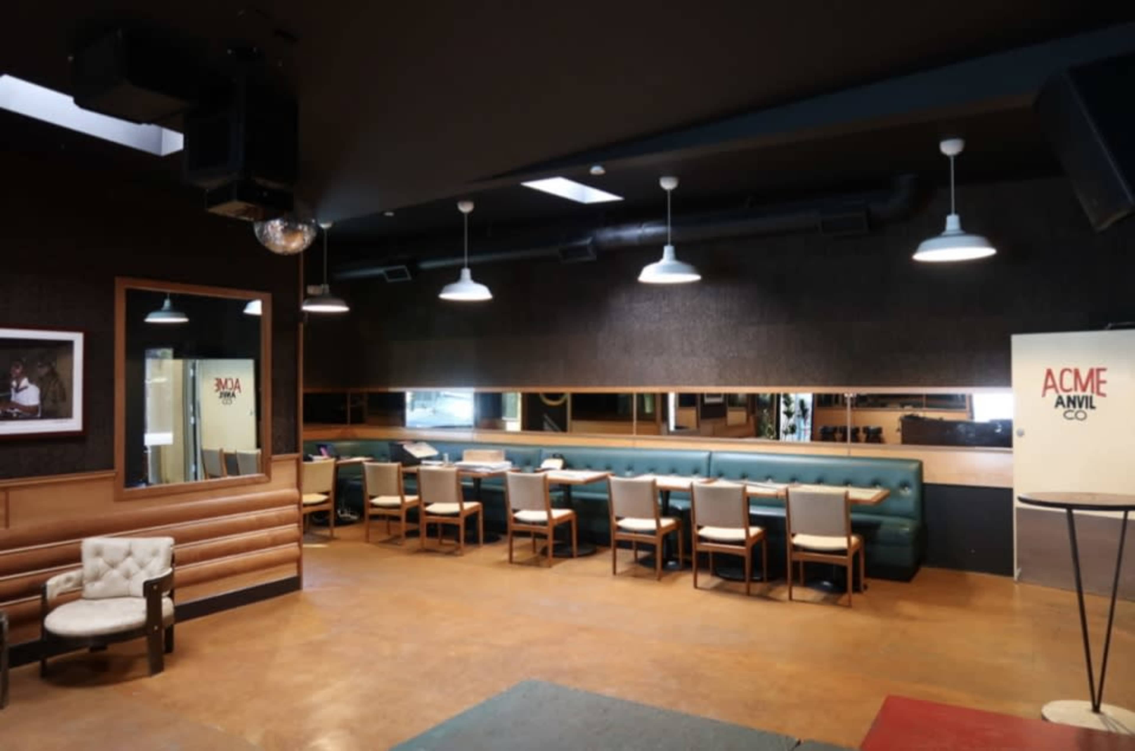 The image shows a modern interior of a restaurant or café with a seating area featuring a long green bench and several tables with chairs, illuminated by pendant lights.