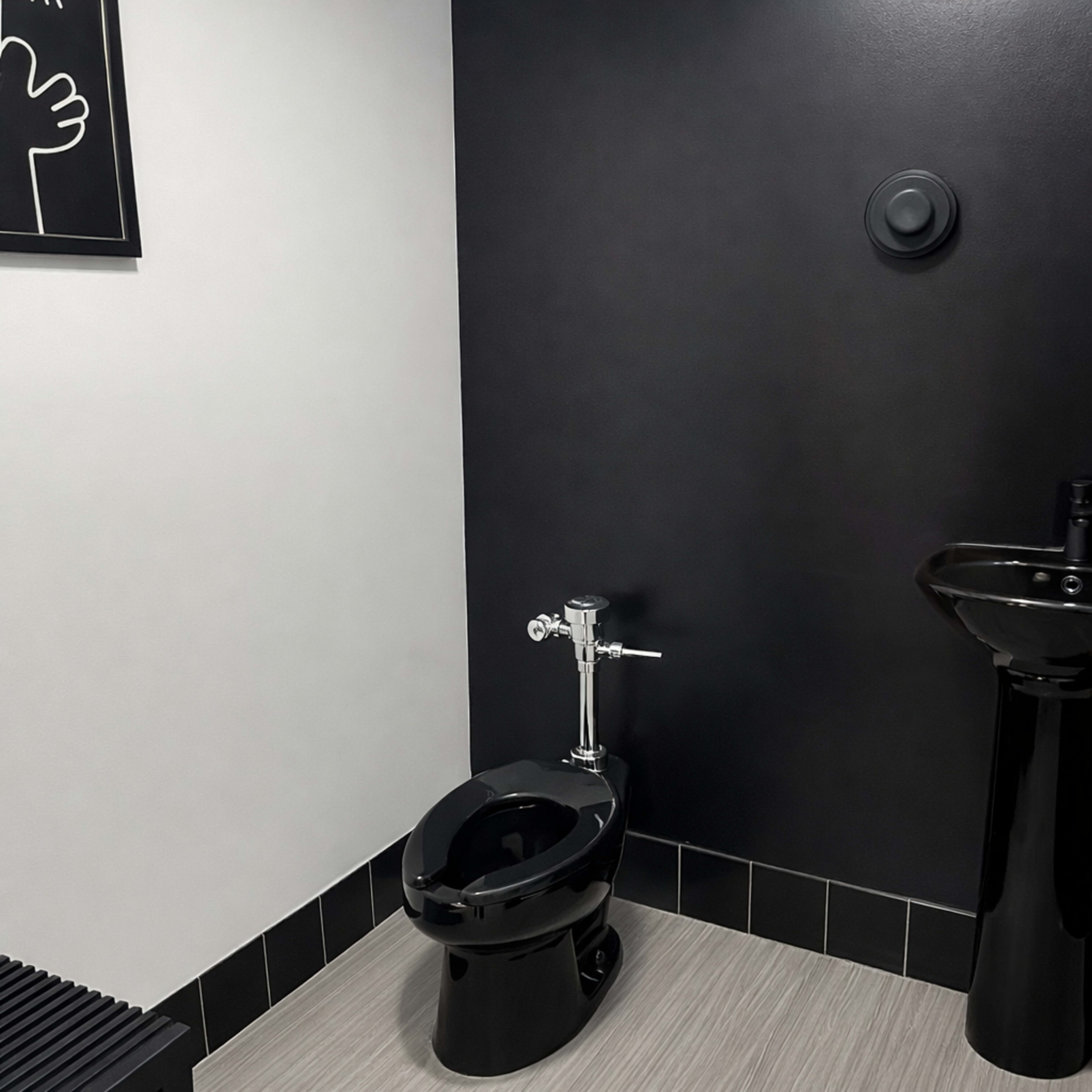 The image shows a modern bathroom featuring a black toilet and a black sink against a two-tone wall of light gray and dark gray.