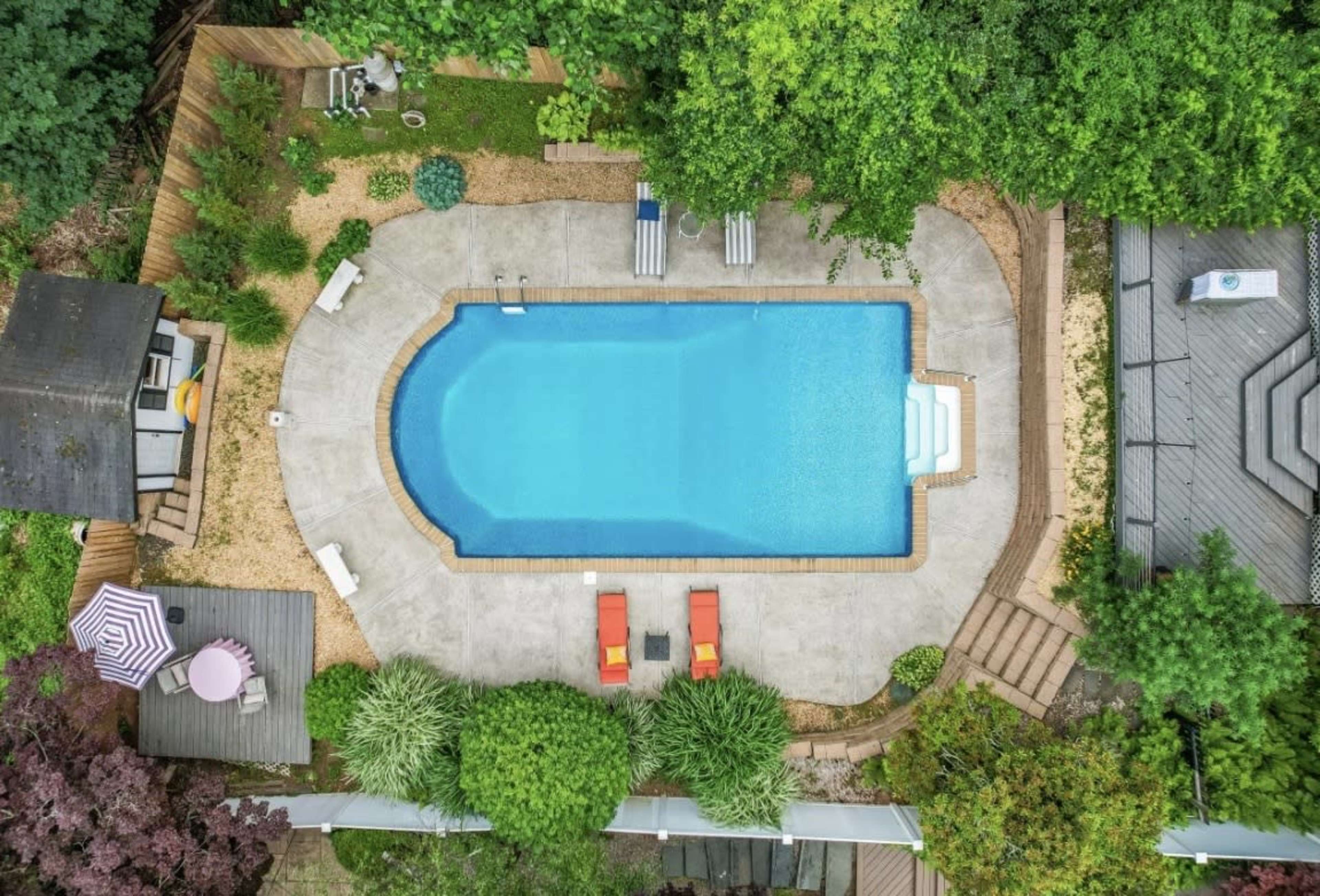 An aerial view of a rectangular swimming pool surrounded by landscaped gardens and seating areas.