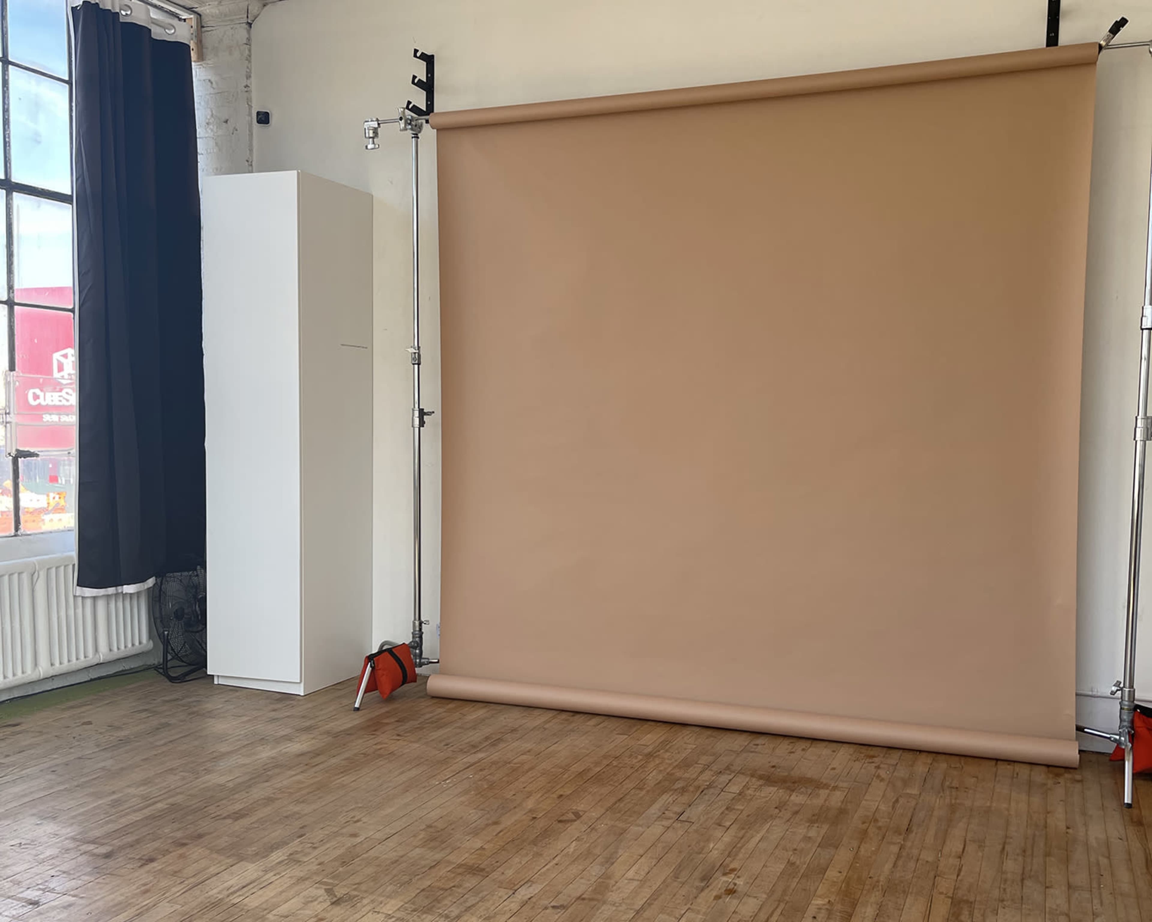 A studio setting with a brown backdrop rolled down, a white storage unit, and large windows letting in natural light.