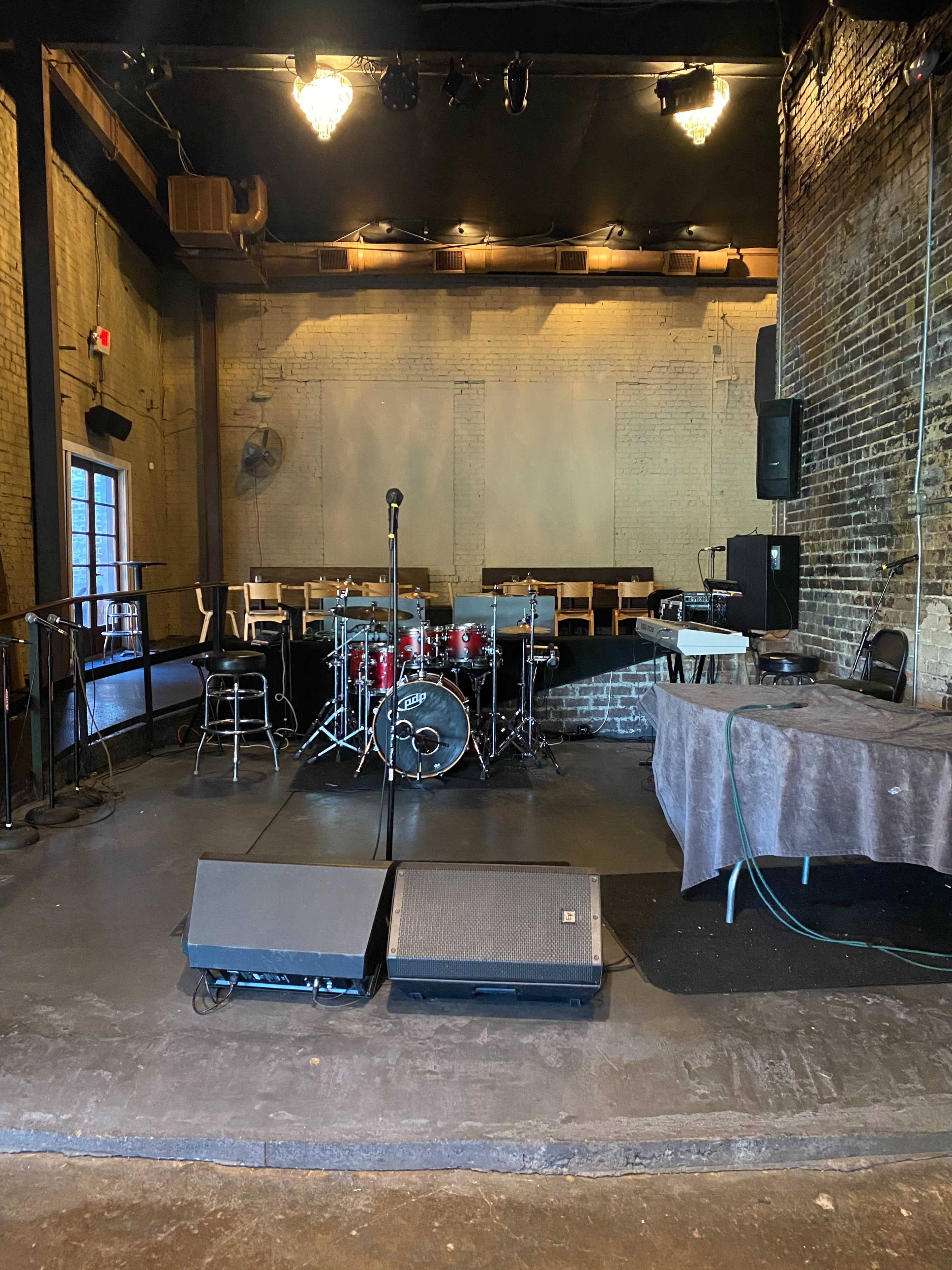 A stage setup in a music venue, featuring a drum kit, microphones, and various audio equipment.
