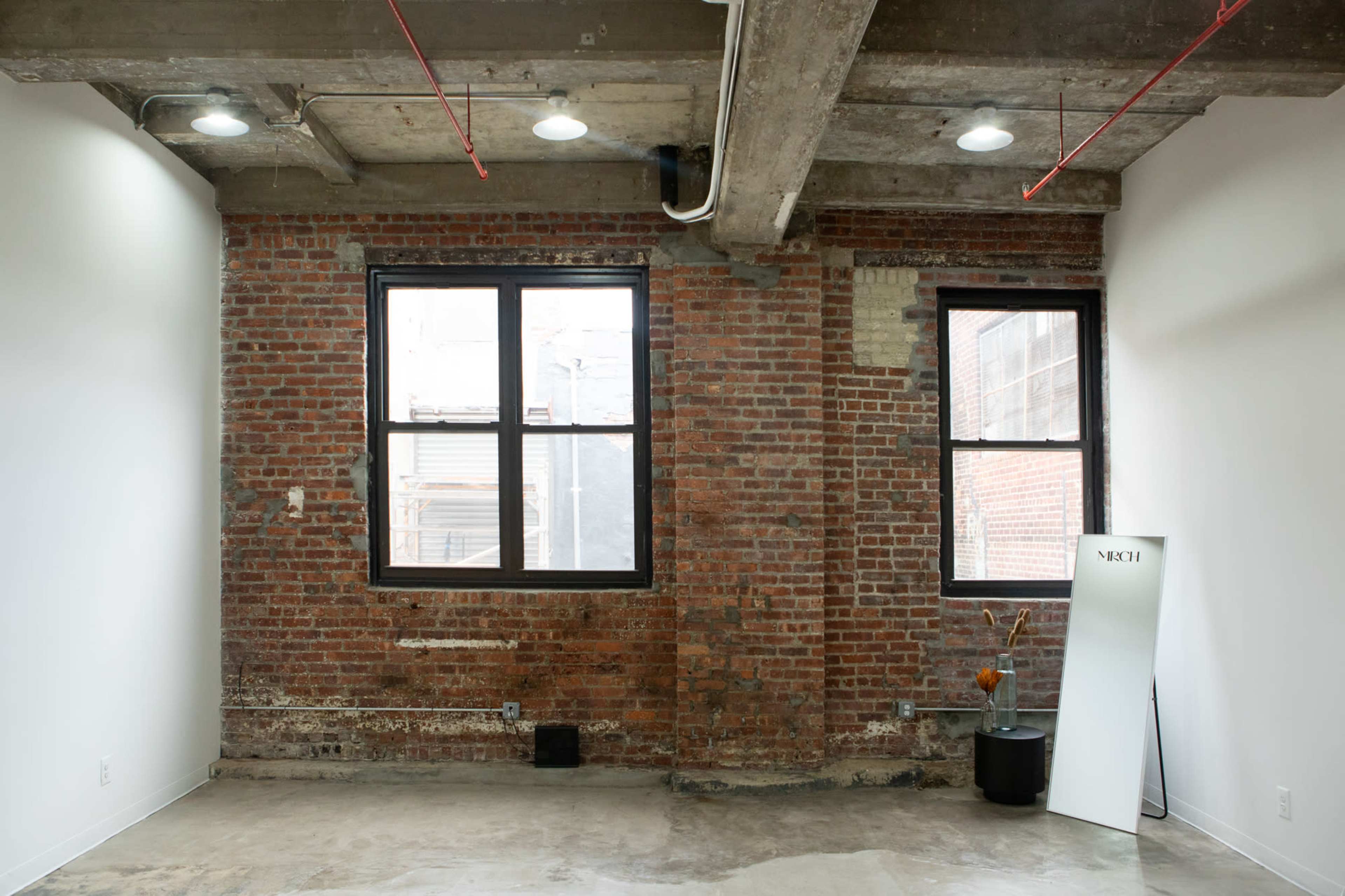 An industrial-style interior with exposed brick walls, large windows, and a concrete ceiling.
