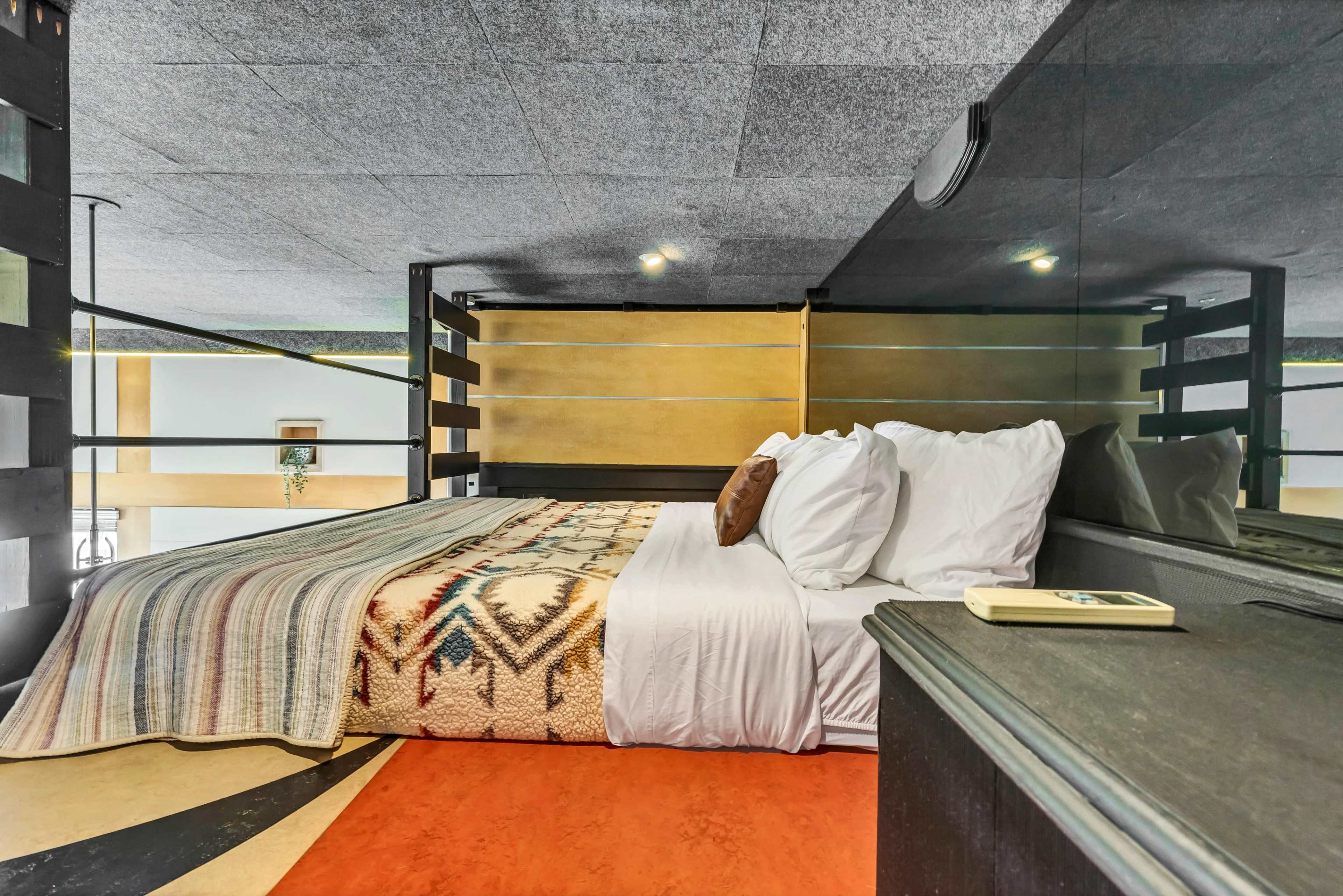 A modern bedroom with a large bed featuring patterned blankets, a wooden bedside table, and a dark color scheme.