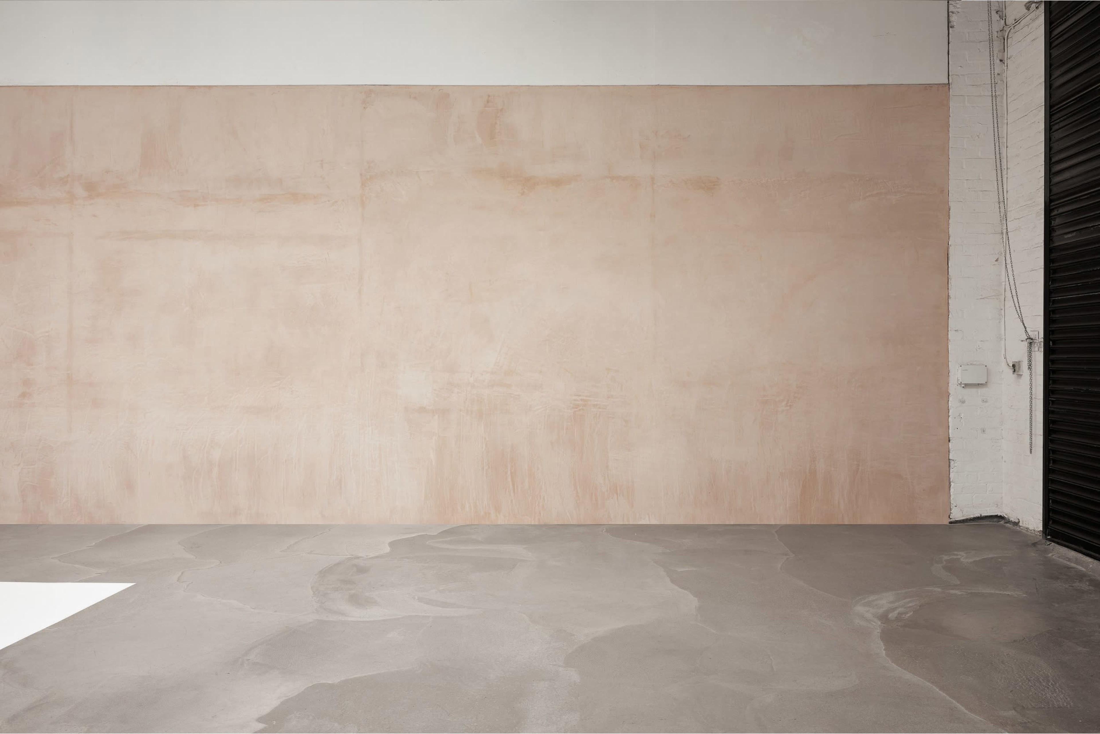 A large, light peach-colored wall beside a floor with a smooth gray surface, set in a minimalist interior space.