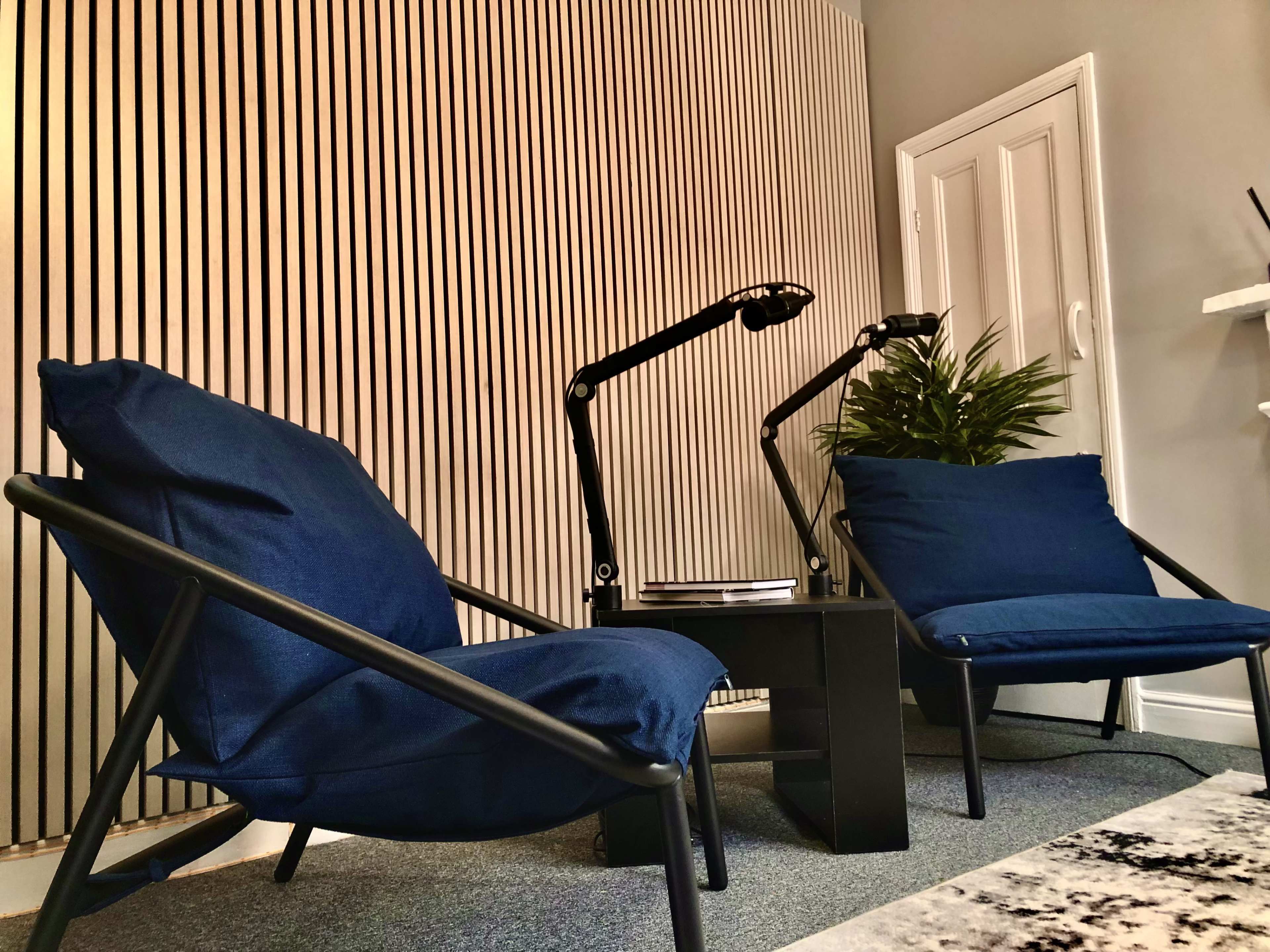 Two blue chairs with black metal frames are positioned facing each other, accompanied by a small black table and two adjustable desk lamps against a striped wall.