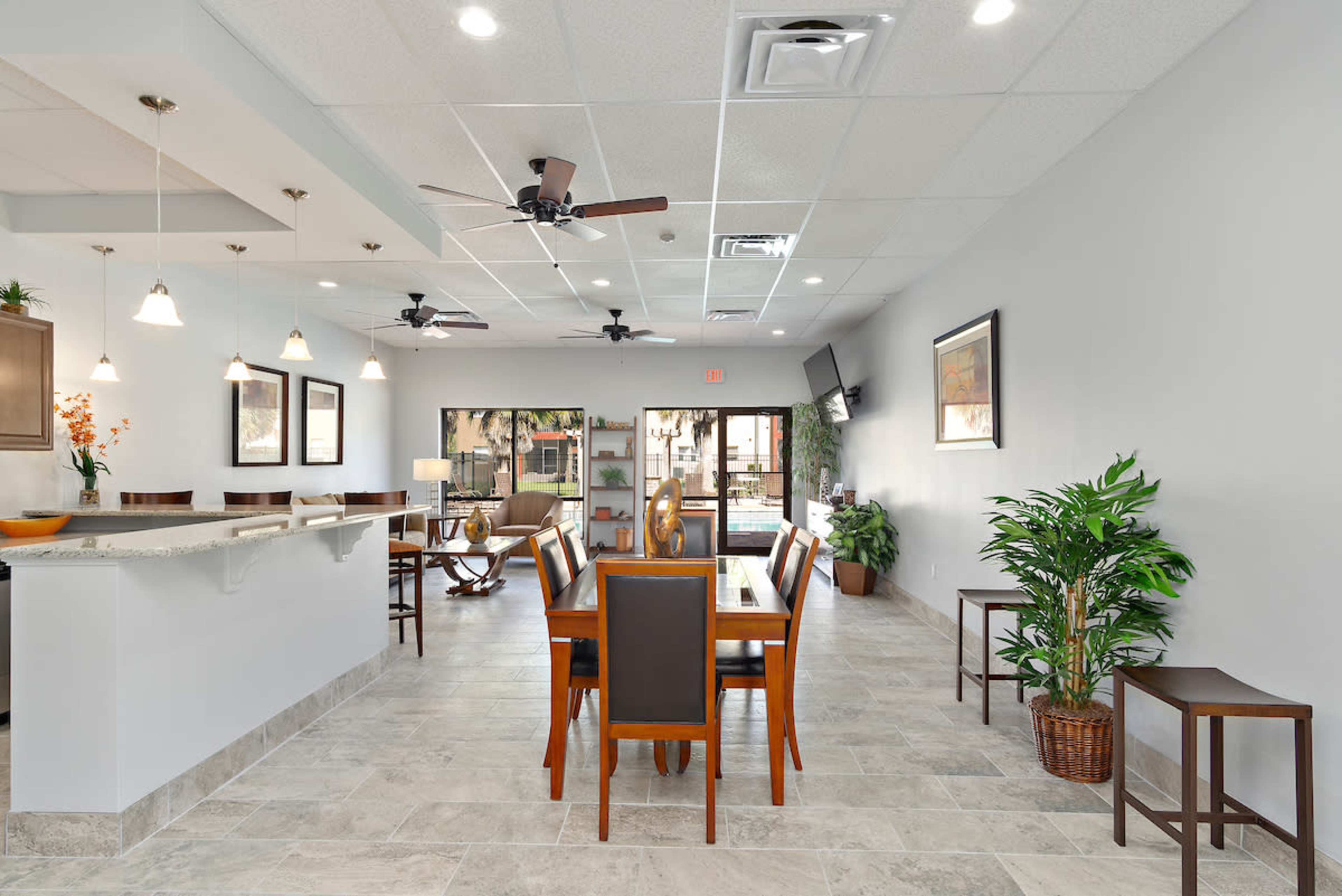 A modern dining area with a central wooden dining table, chairs, ceiling fans, and large windows leading to an outdoor space.