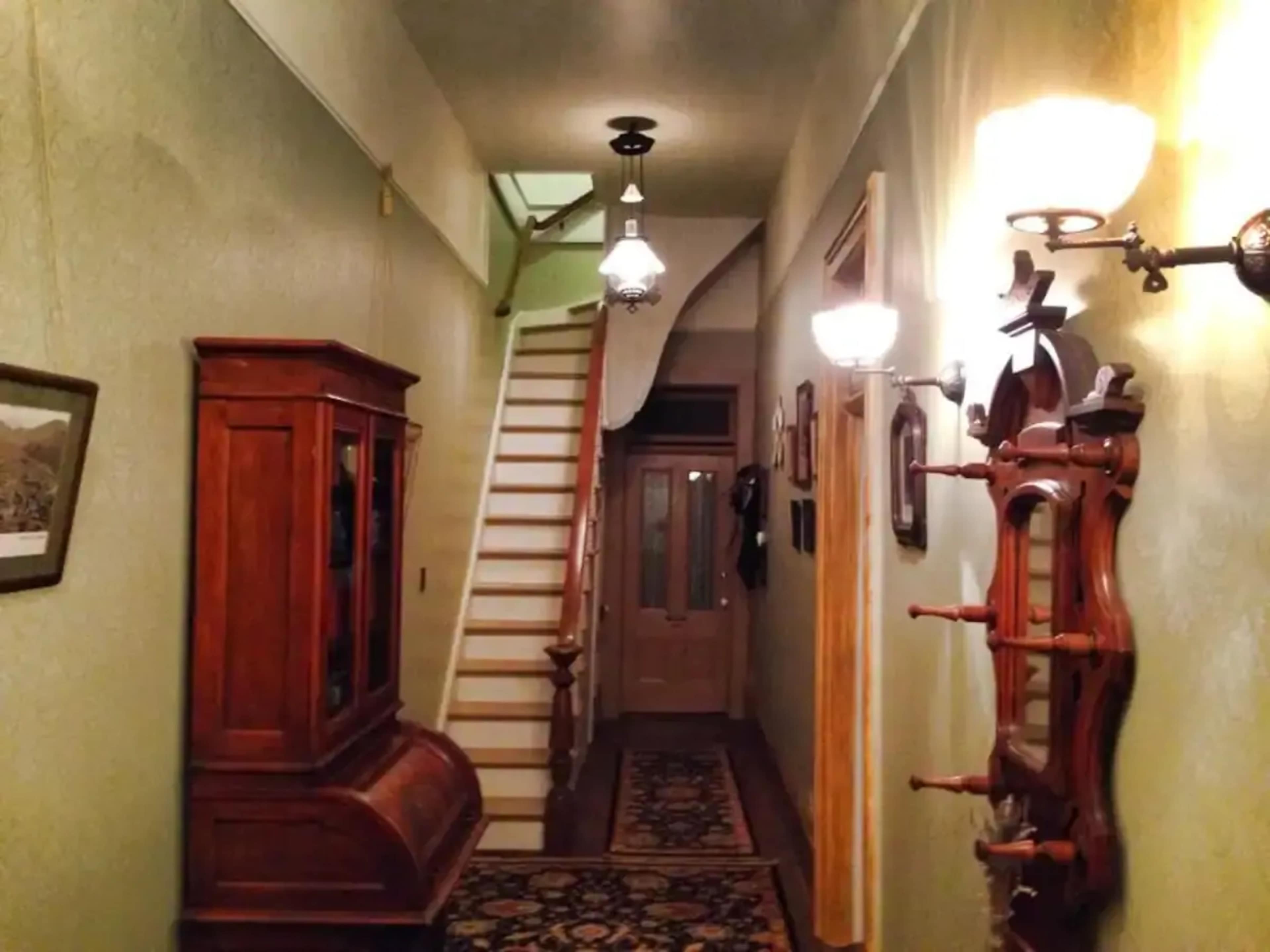 A narrow hallway features a staircase at the end, flanked by wooden furniture and wall-mounted light fixtures.