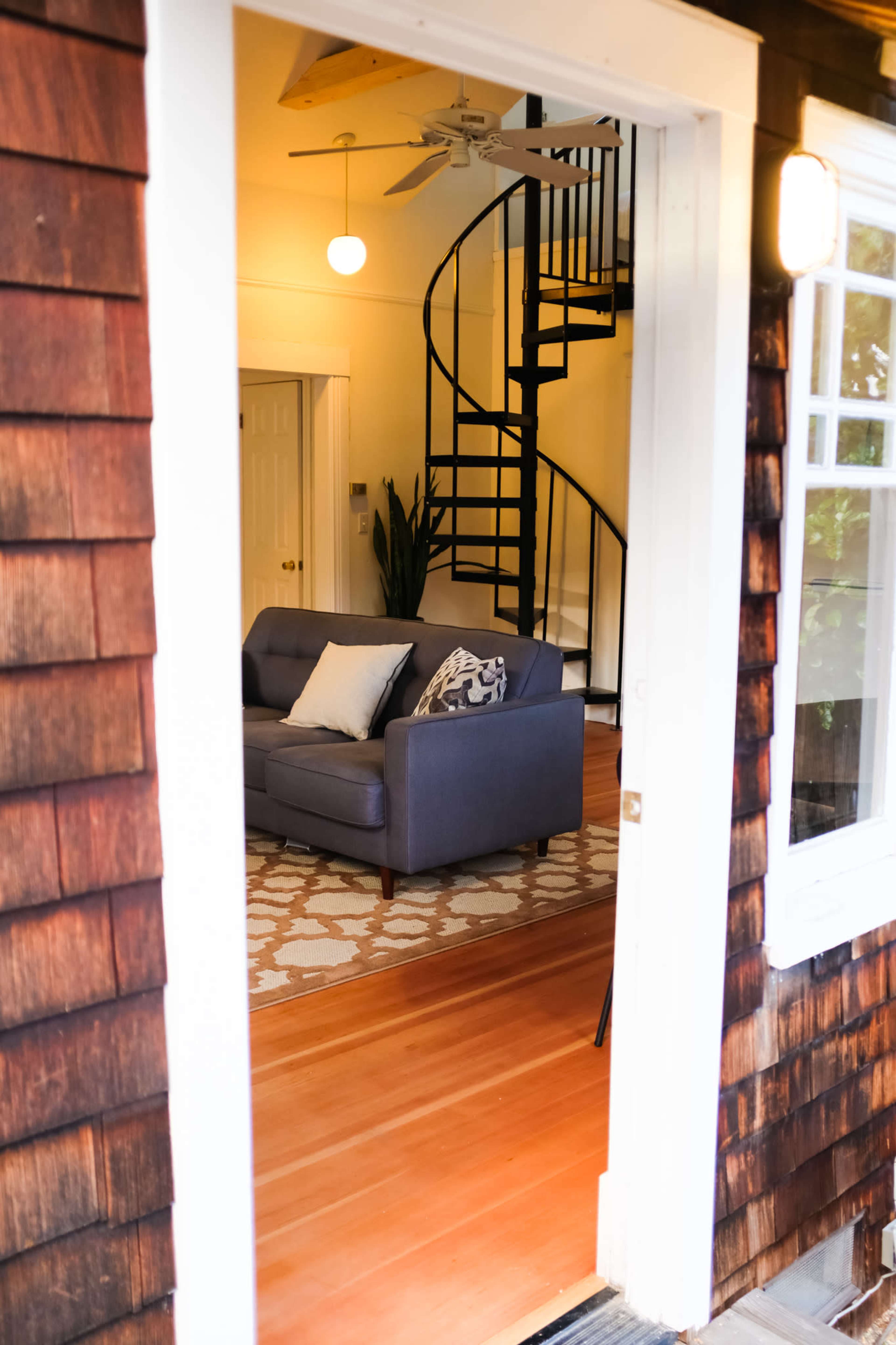 A doorway frames a view of a living room with a spiral staircase and a blue couch.